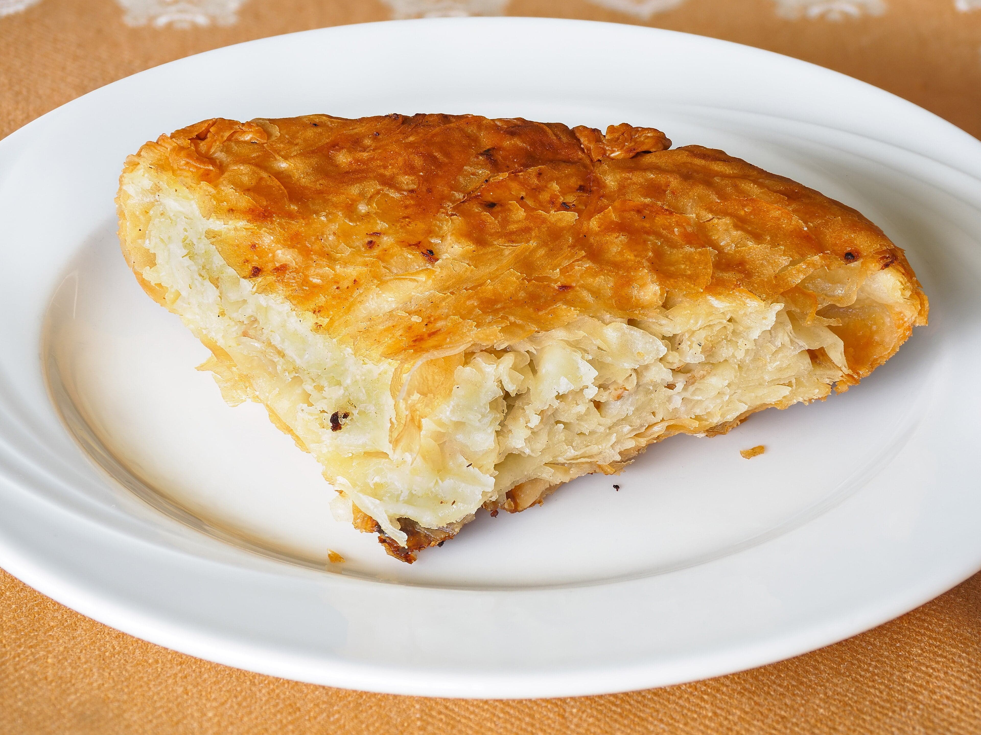A tray of golden flaky byrek pastry being cut into squares