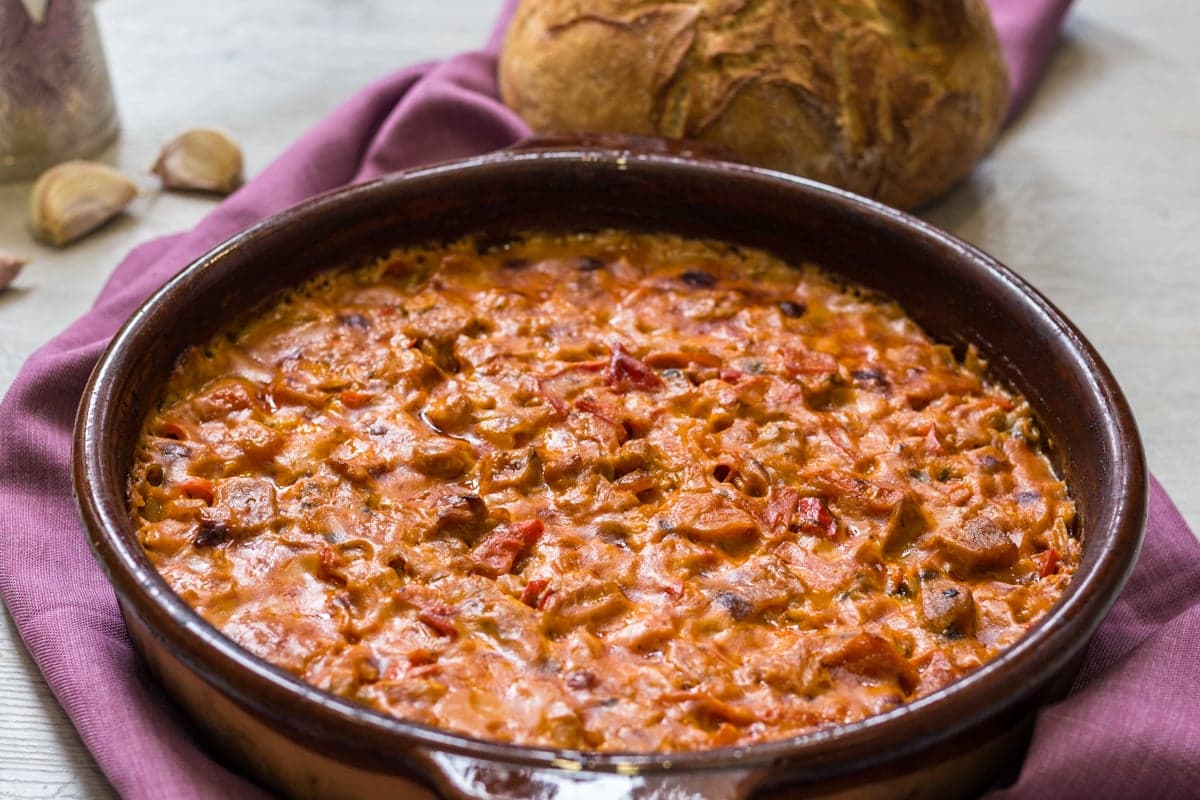 A clay dish of fërgesë with red peppers, tomato and white cheese