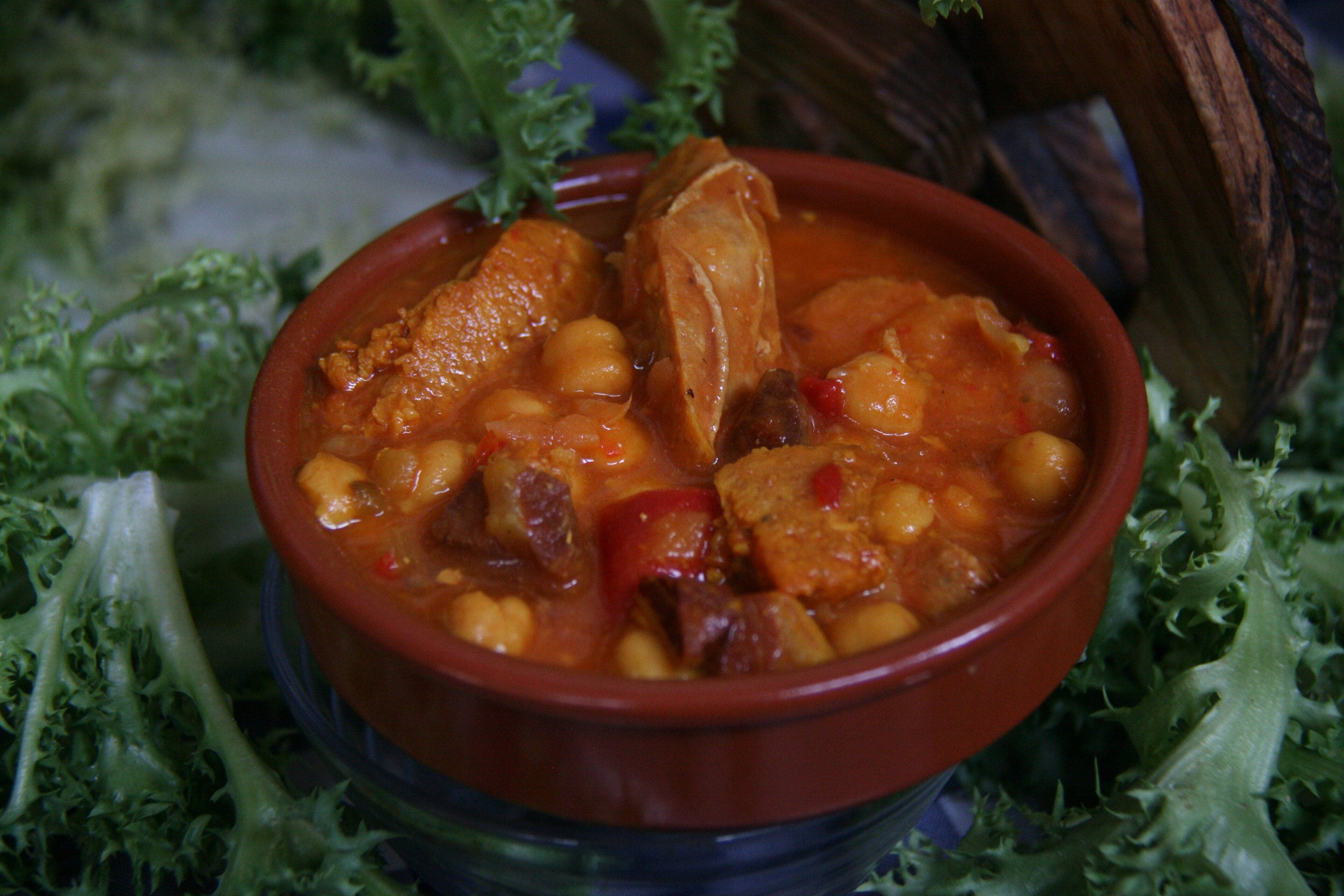 A steaming bowl of escudella stew with pasta and vegetables on a wooden table