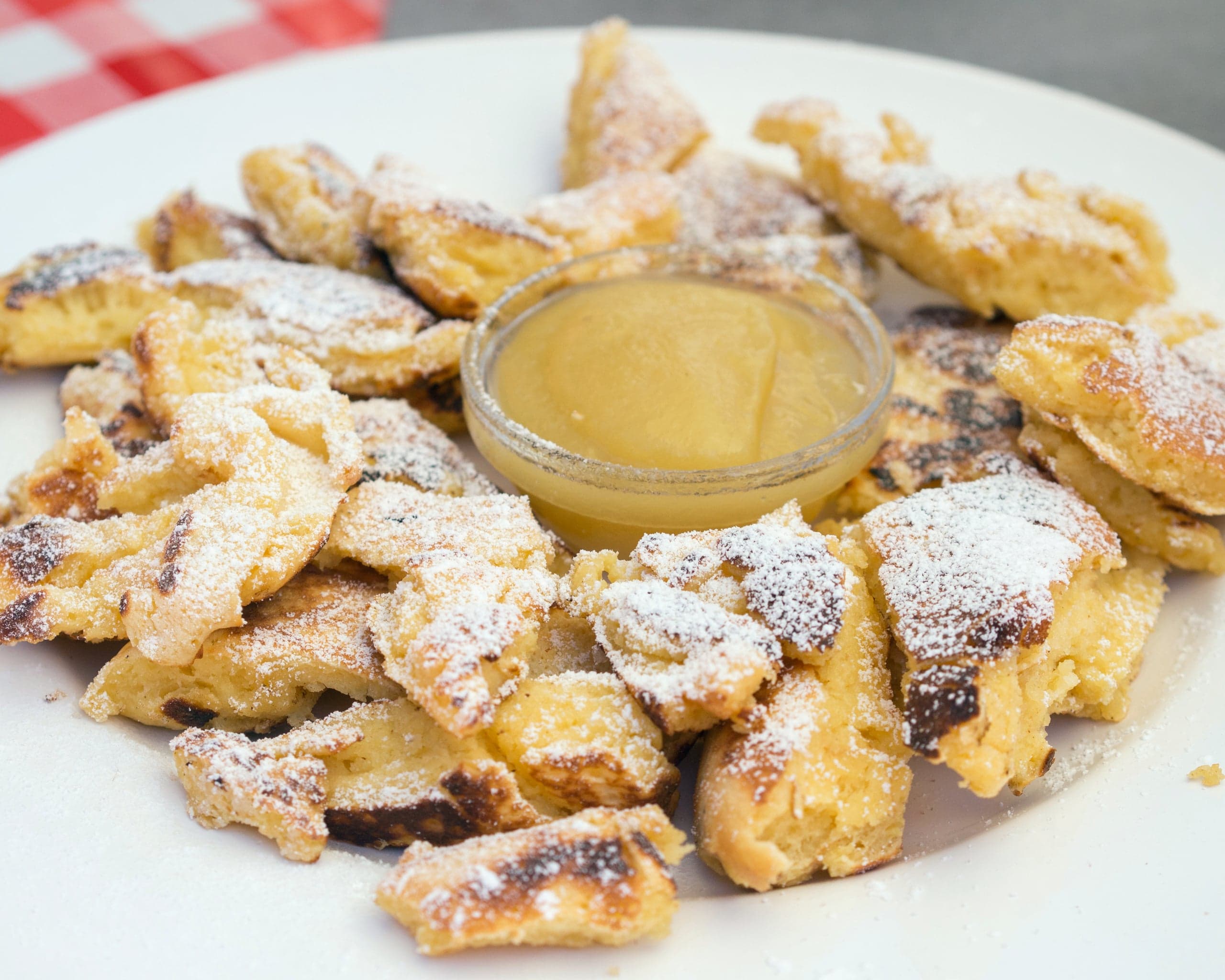 A plate of fluffy torn Kaiserschmarrn dusted with icing sugar and served with plum sauce