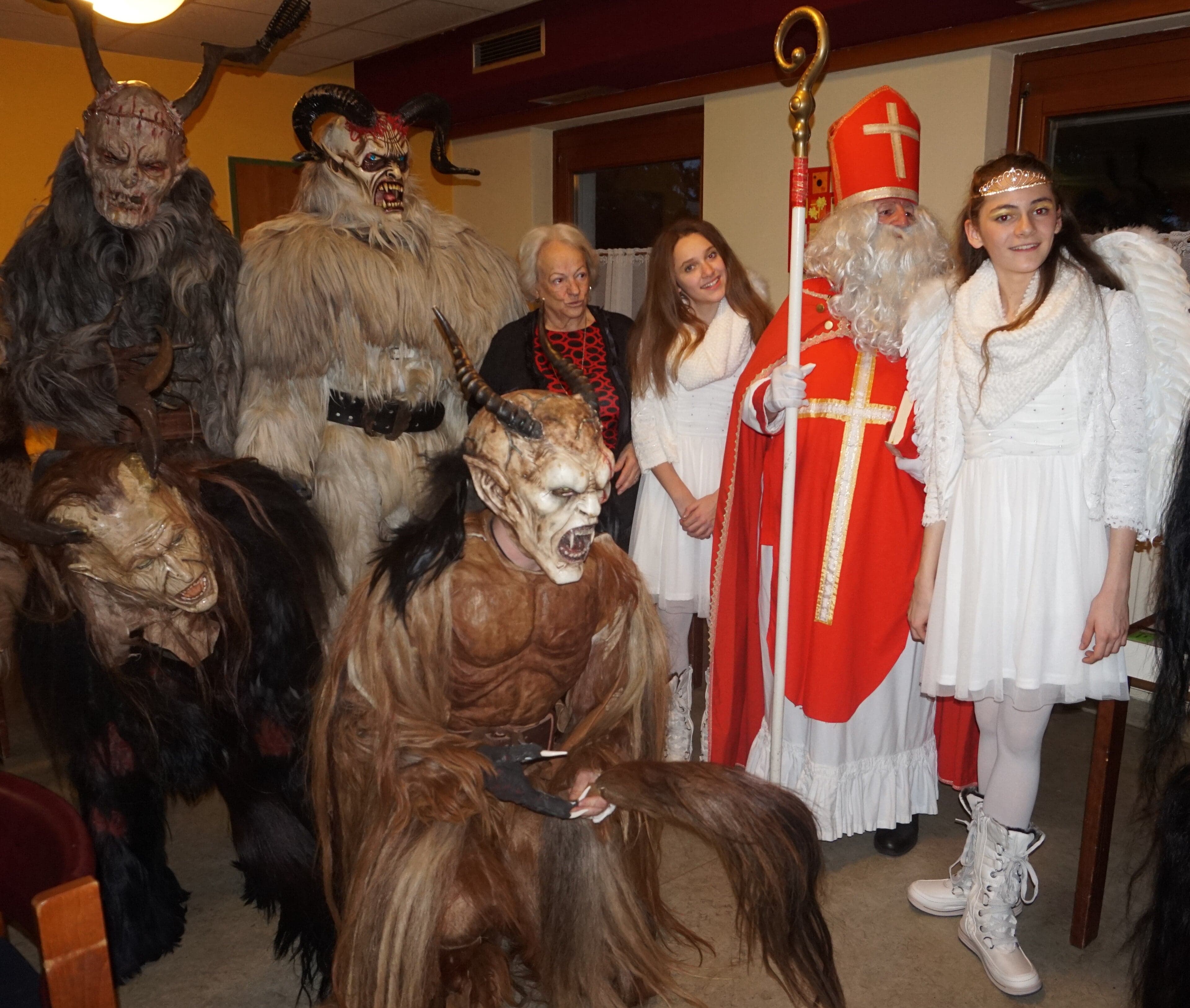 Performers in elaborate horned Krampus costumes with bells and furry suits marching through a town square
