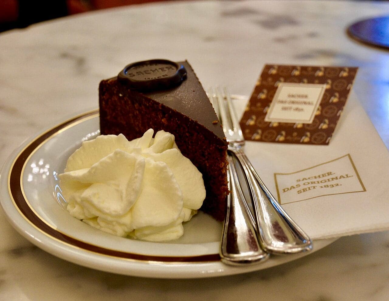 A slice of dark chocolate Sachertorte with a layer of apricot jam and a cup of coffee beside it