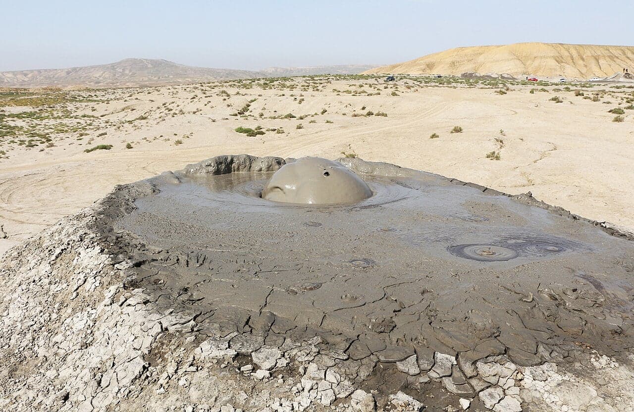 A small mud volcano with grey mud bubbling out of its cone on a dry plain in Azerbaijan