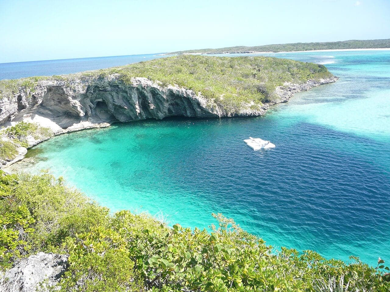 A deep circular blue hole seen from above in shallow turquoise water