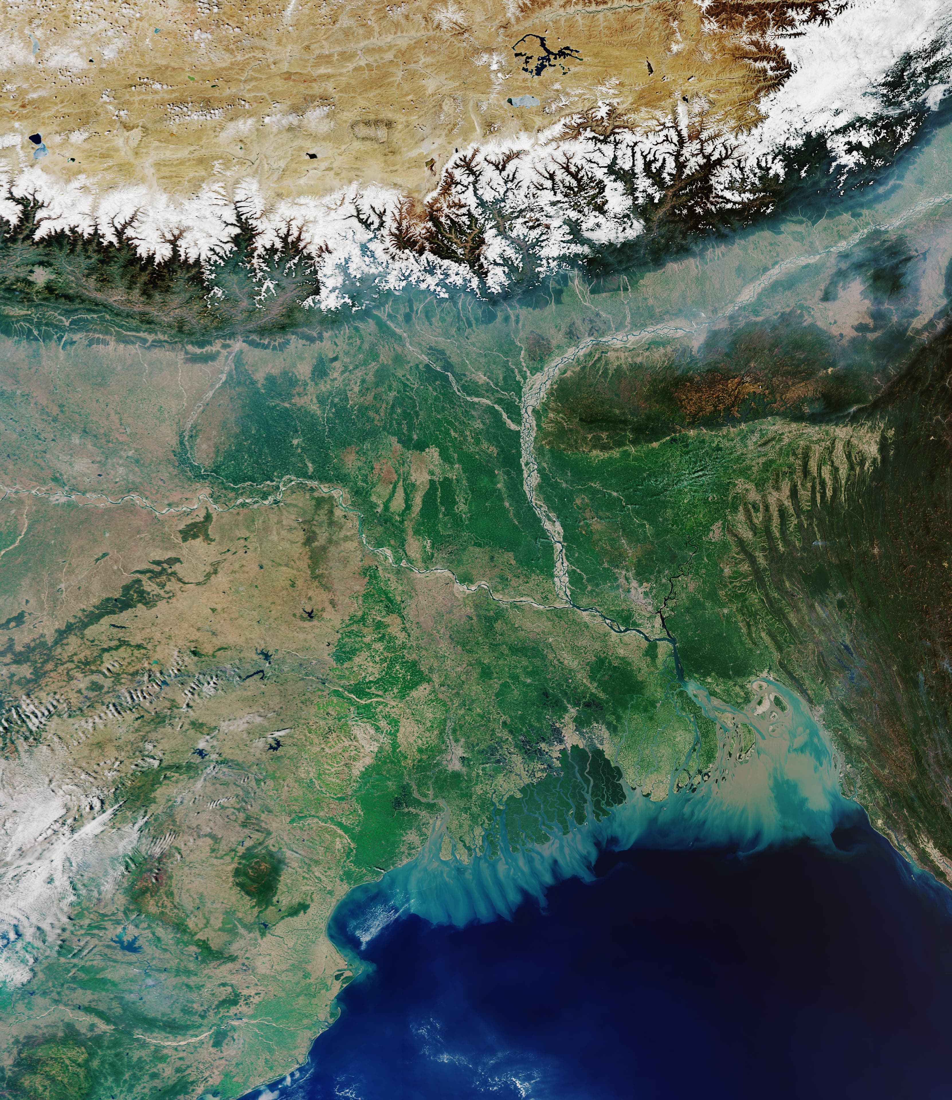 A satellite view of the Ganges-Brahmaputra delta, showing green land laced with bright silver rivers reaching the sea