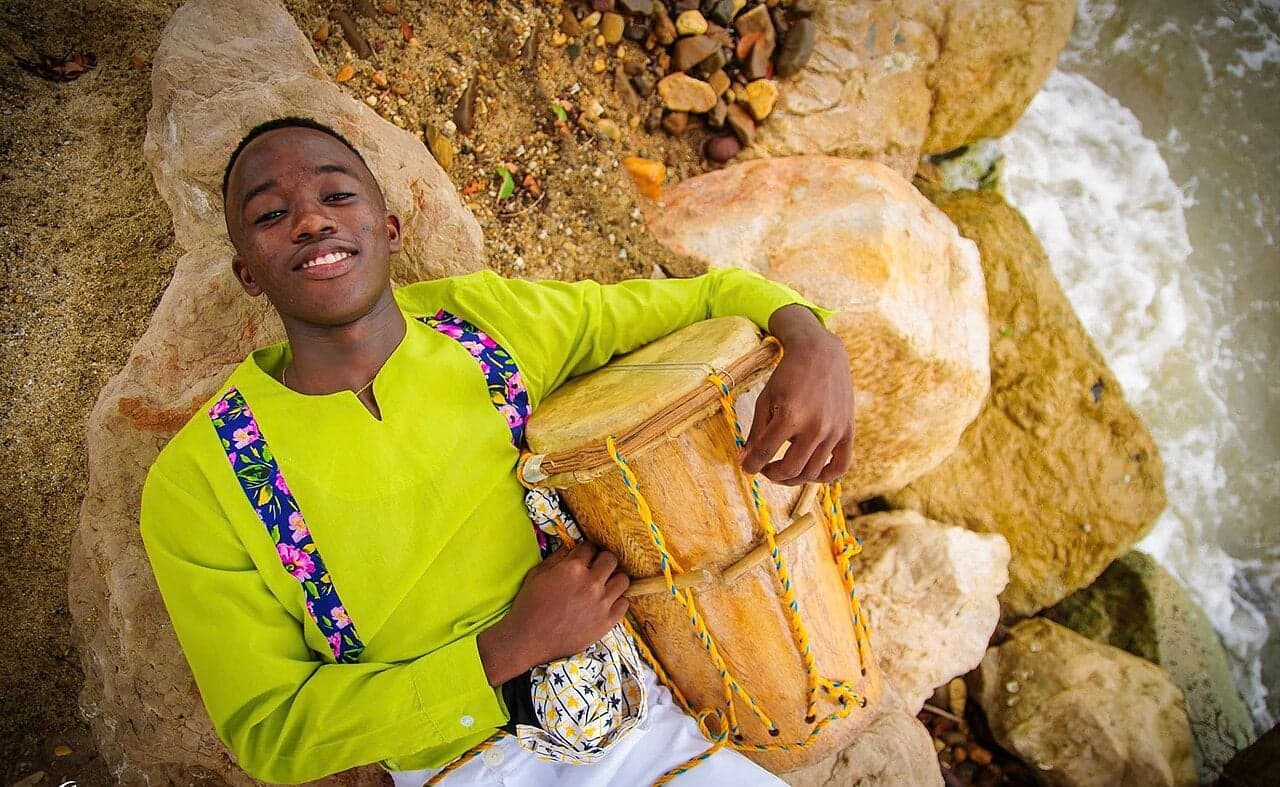 A Garifuna drummer playing a large hand drum at a colourful outdoor celebration