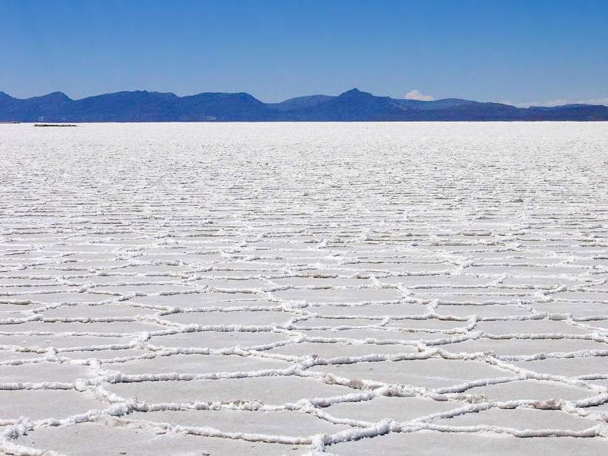 A perfectly flat white salt plain reflecting a blue sky and clouds like a giant mirror