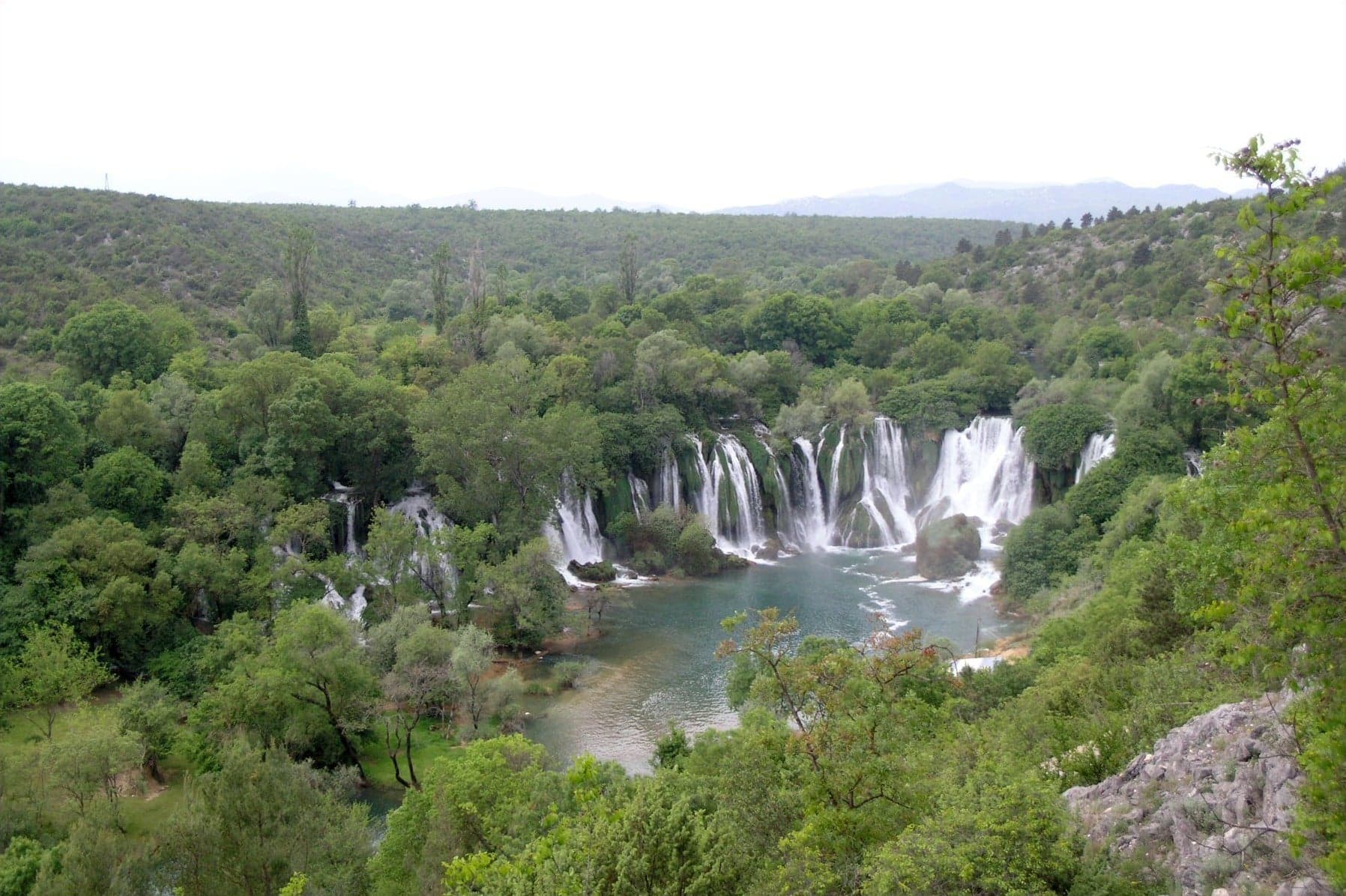 The wide horseshoe of Kravica Waterfalls tumbling into a turquoise pool surrounded by lush vegetation