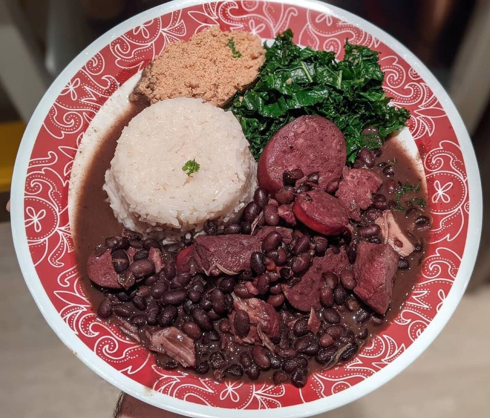 A bowl of feijoada with black beans, rice, greens and farofa