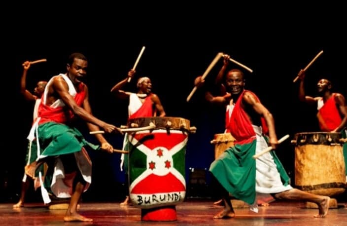 A group of Burundian royal drummers in white costumes playing tall drums outdoors