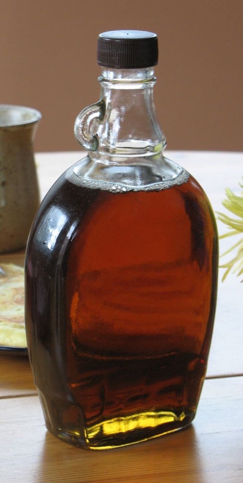 A glass bottle of amber maple syrup on a wooden table