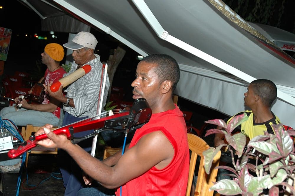 A Cape Verdean singer performing morna in a colourful dress, with guitarists behind
