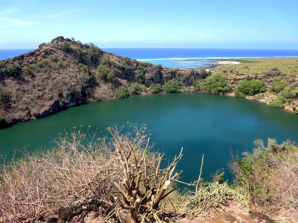 The still waters of Lac Salé crater lake surrounded by green vegetation on Grande Comore