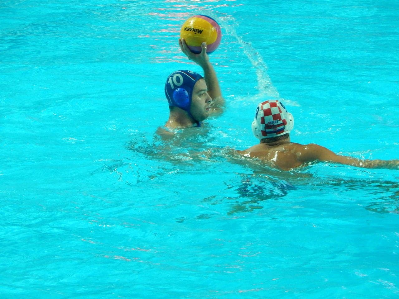 Water polo players in a pool, one player throwing a ball towards the goal