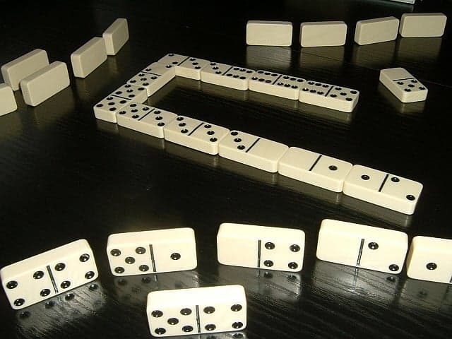 Four men sitting around a wooden table playing dominoes under a shade tree