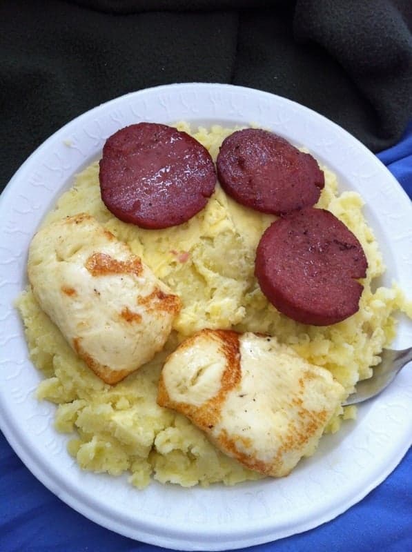 A bowl of mangú - mashed green plantain - topped with sautéed onions, beside sliced fried plantain