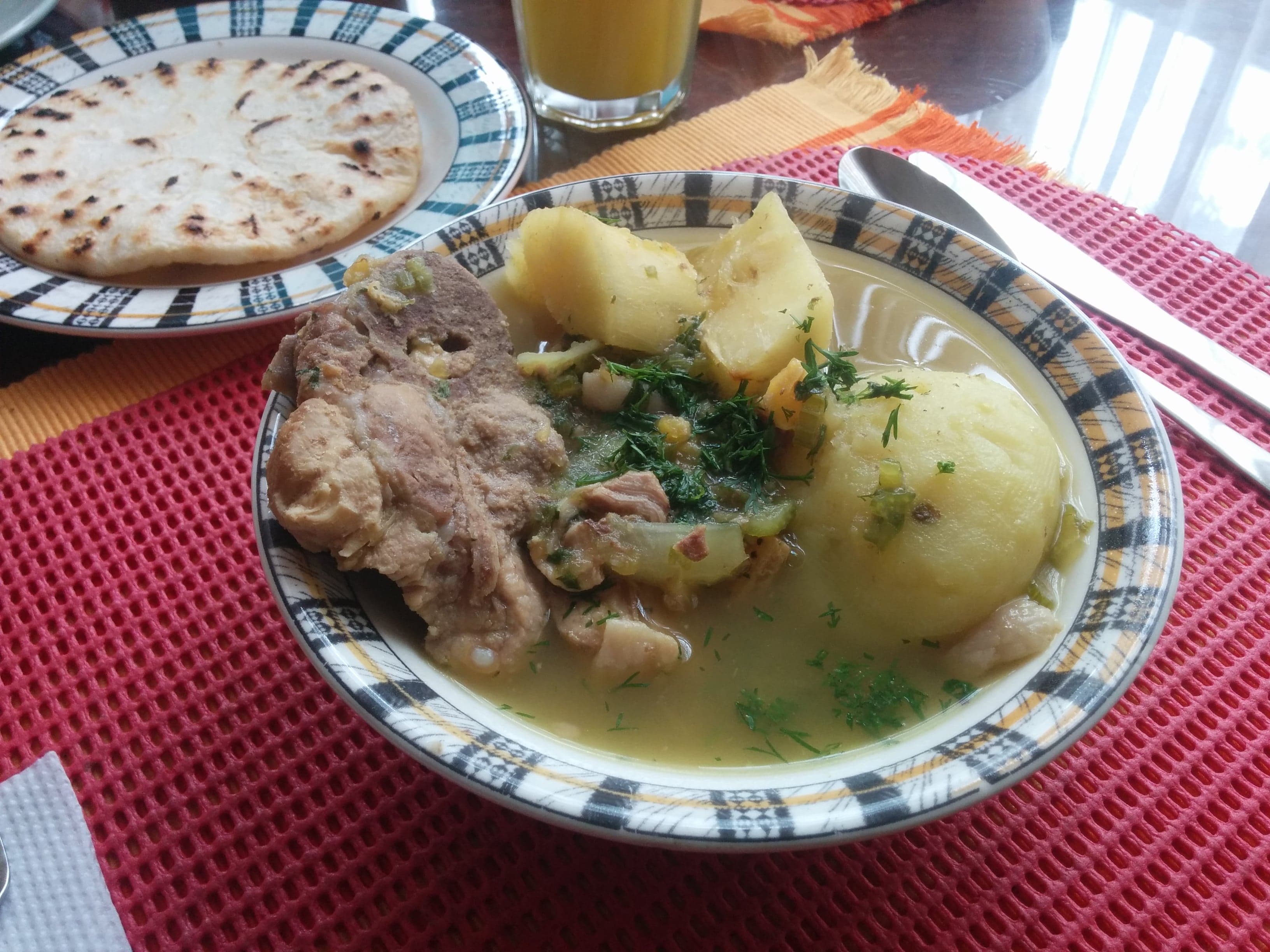 A large pot of sancocho stew filled with root vegetables, corn and meat on a wooden table