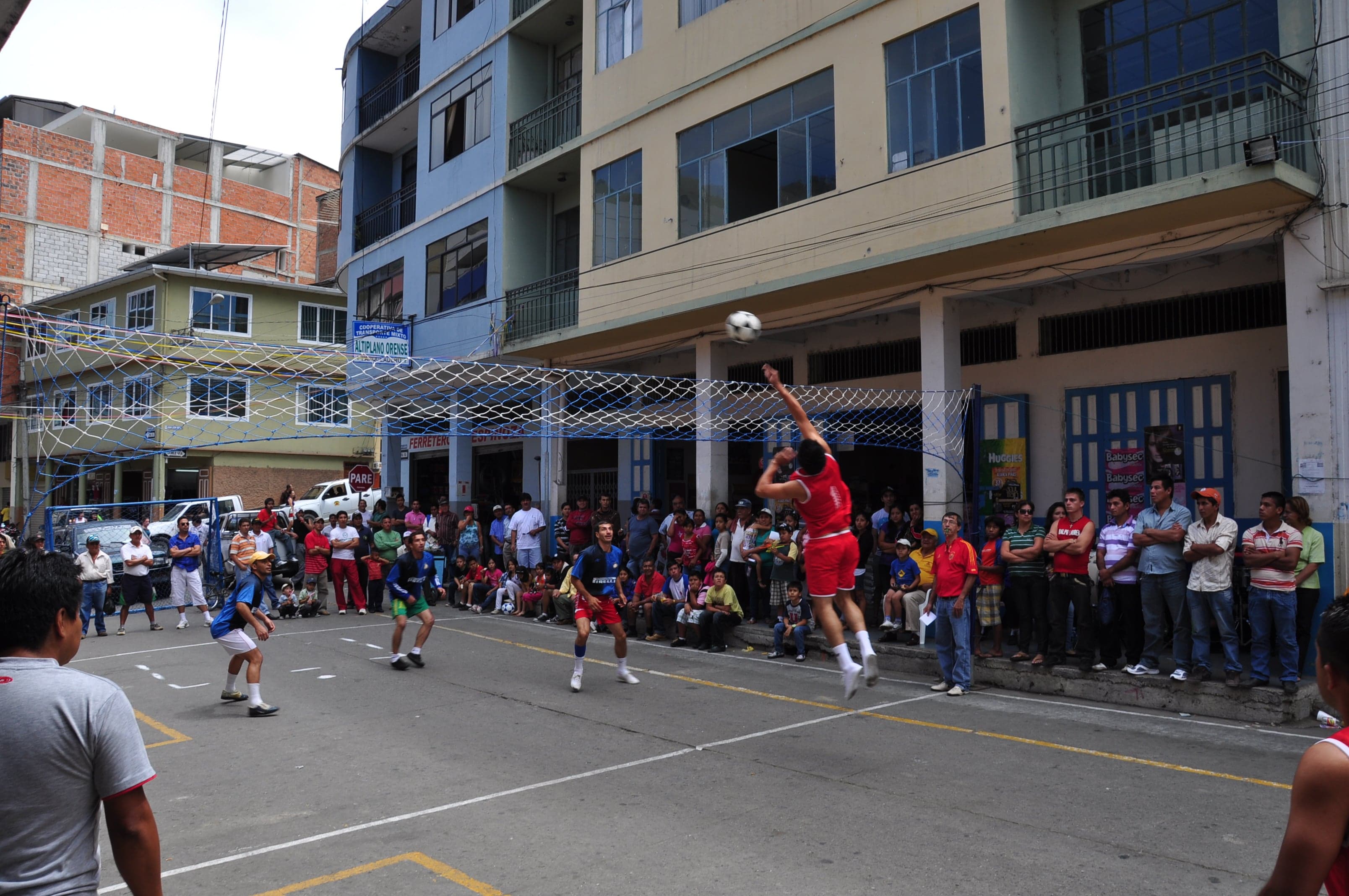 Players jumping to hit a ball over the net during an Ecuavolley match on a street court
