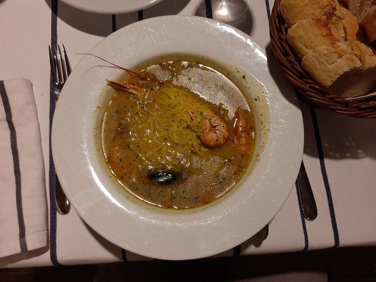 A bowl of rich orange-red fish soup with vegetables and herbs