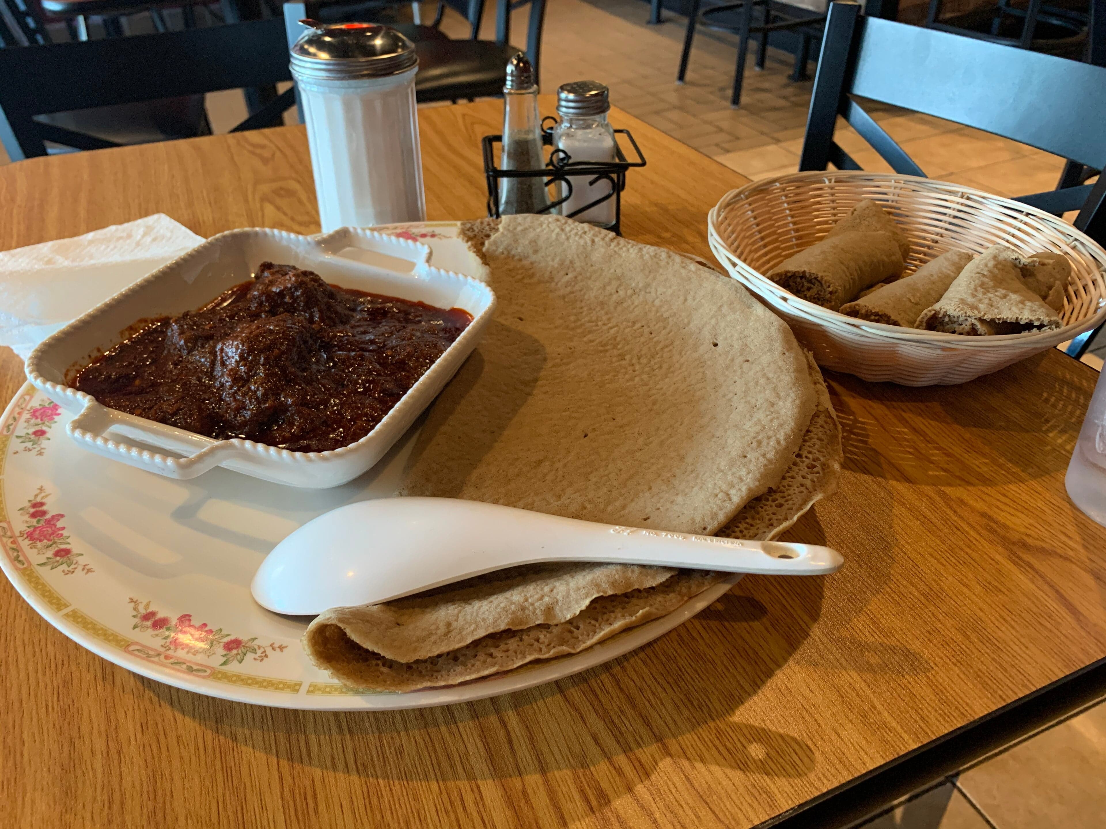 A large round injera flatbread with colourful stews and lentils arranged on top, ready to share