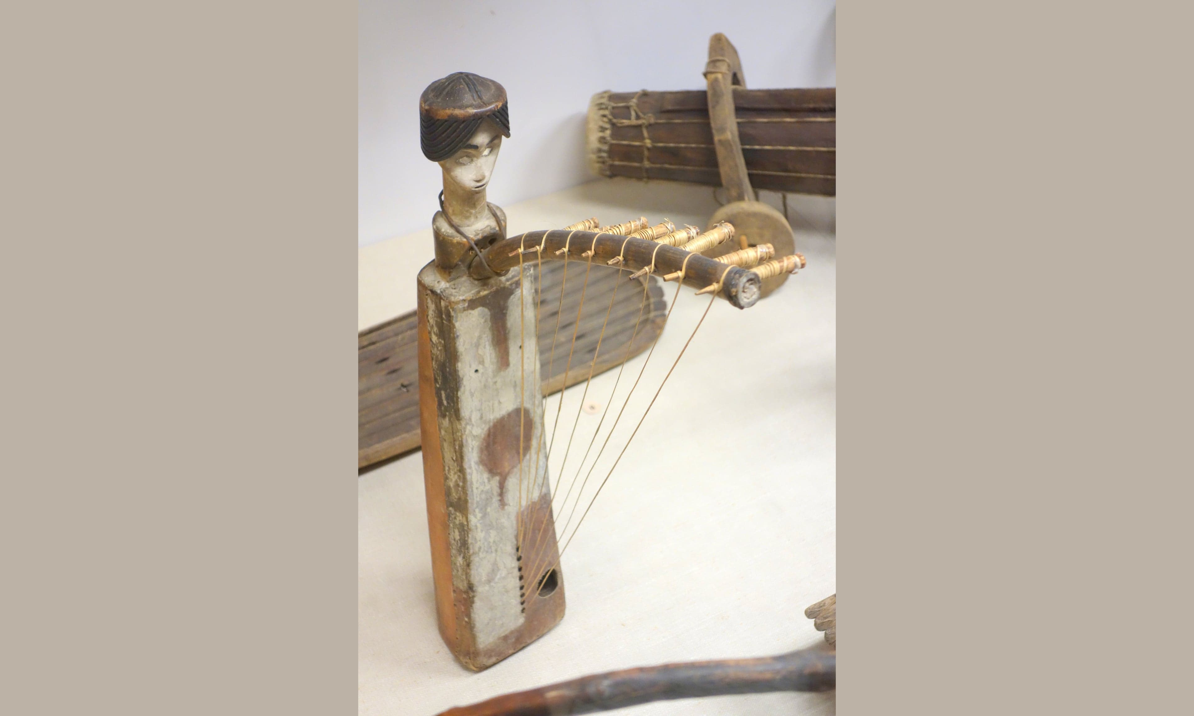 A mvet bow harp made of carved wood and strings, held by a musician