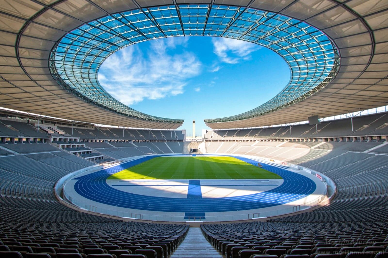 A large empty football stadium with blue running track and green pitch