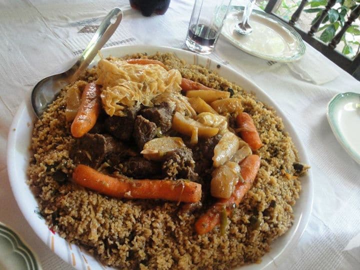 A large pot of riz au gras - rich orange-red rice with pieces of chicken - served in a bowl