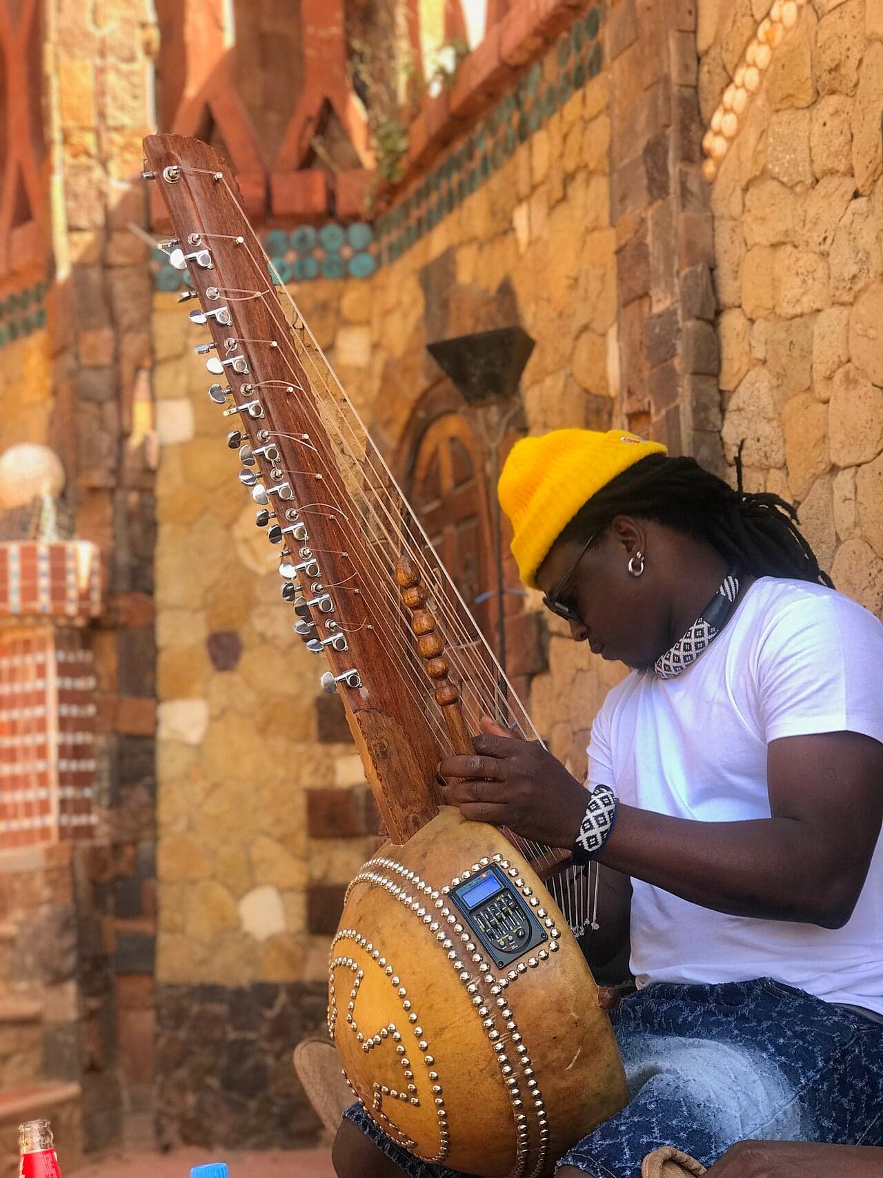 A kora player holding the large gourd instrument with both hands, strings gleaming in the light