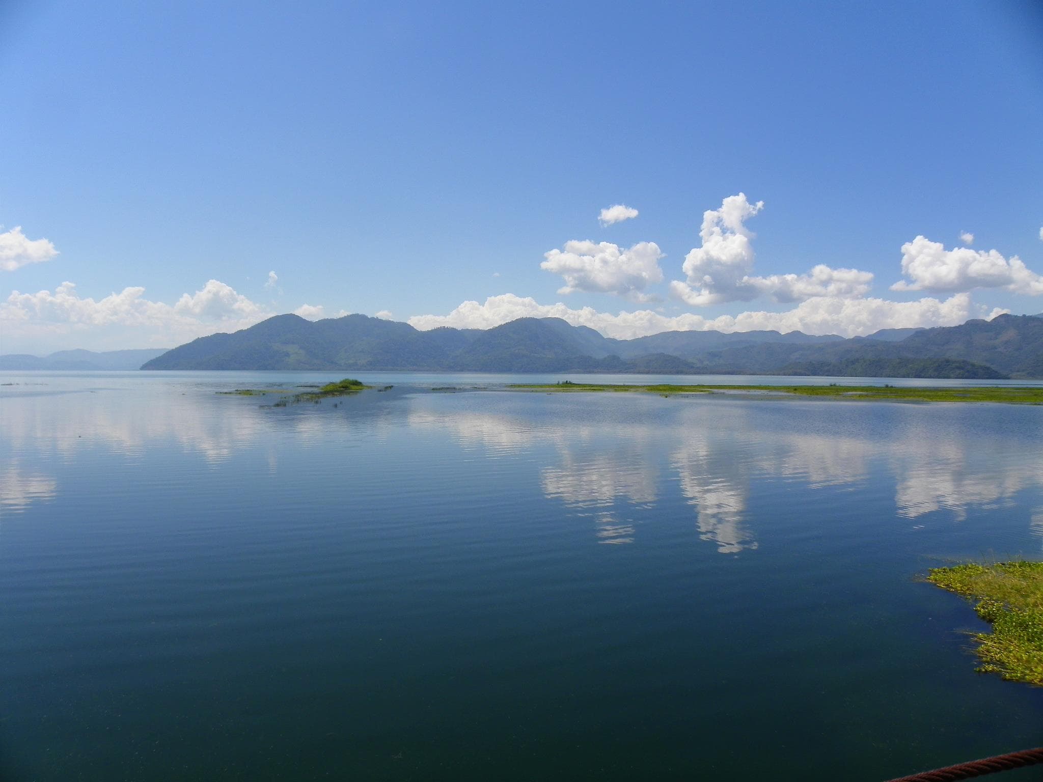 Calm water of Lago Yojoa with lush green mountains and mist in the background, Honduras