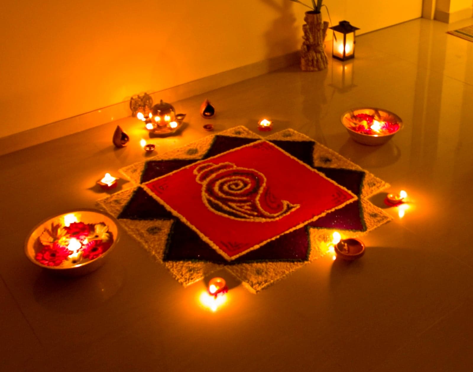 A beautiful rangoli pattern on the floor surrounded by small oil lamps (diyas) and flowers for Diwali