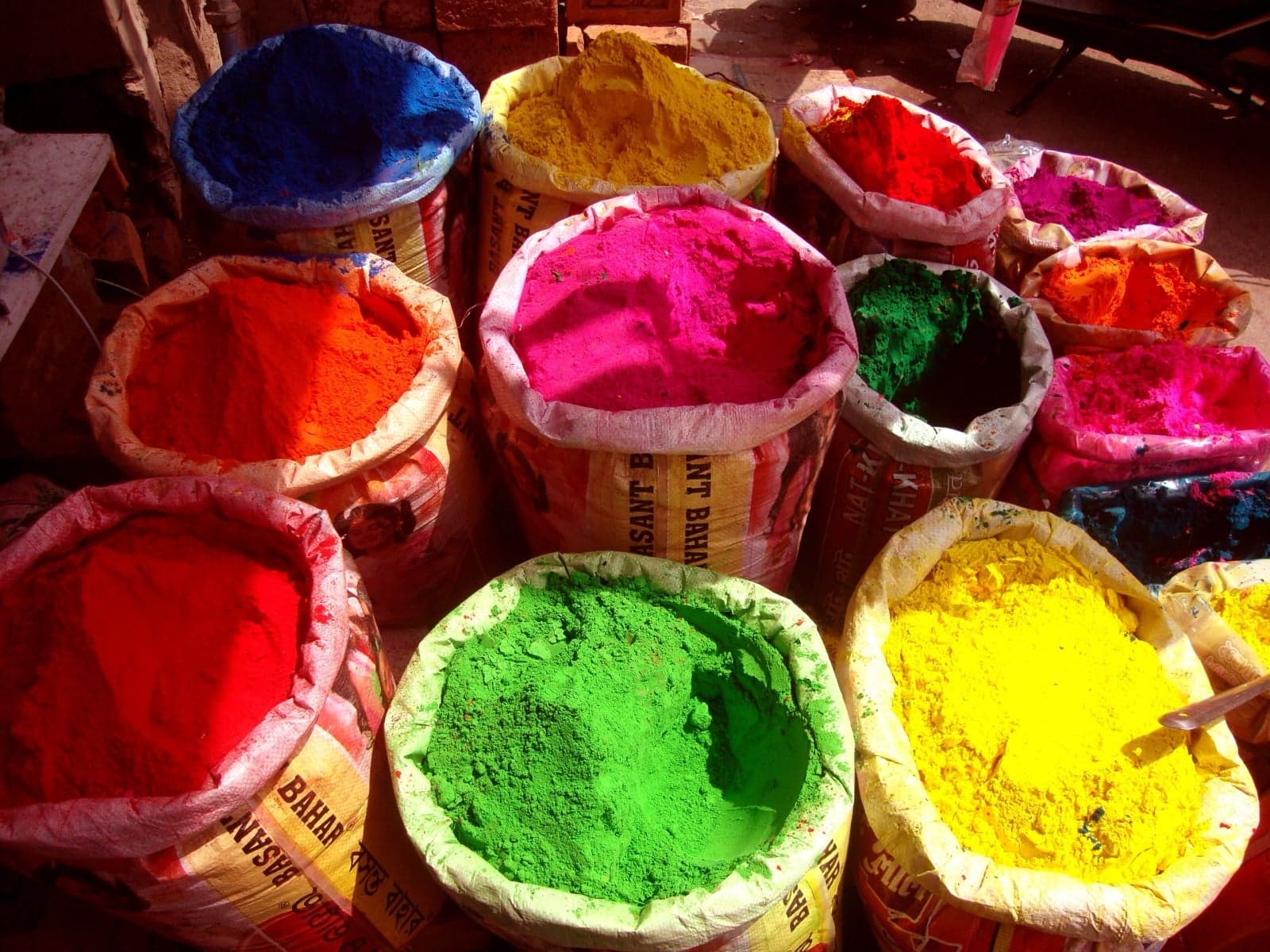 Open sacks of brightly coloured powder for sale at a market - pink, blue, yellow, green and orange