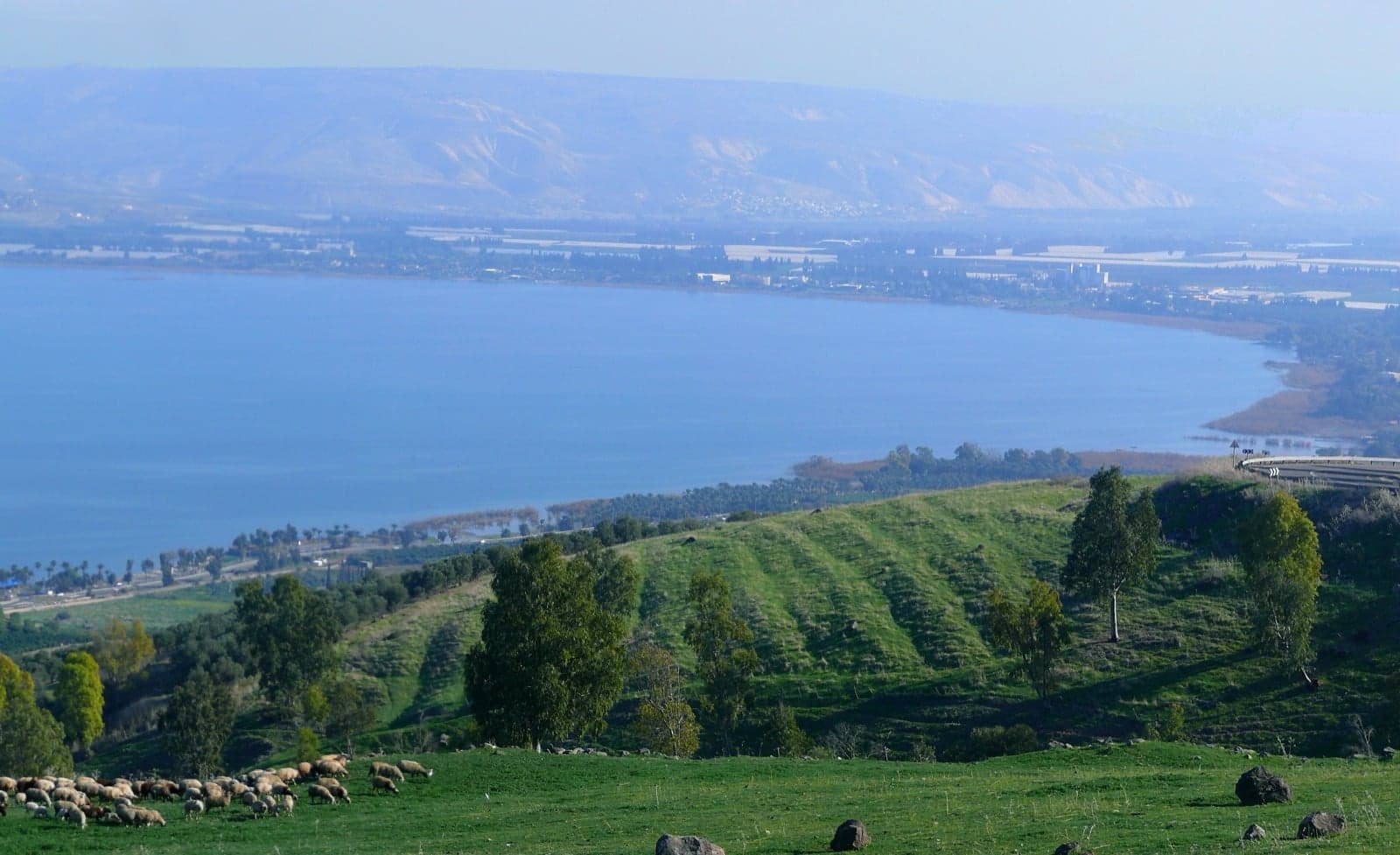 Calm blue water of the Sea of Galilee with green hills behind