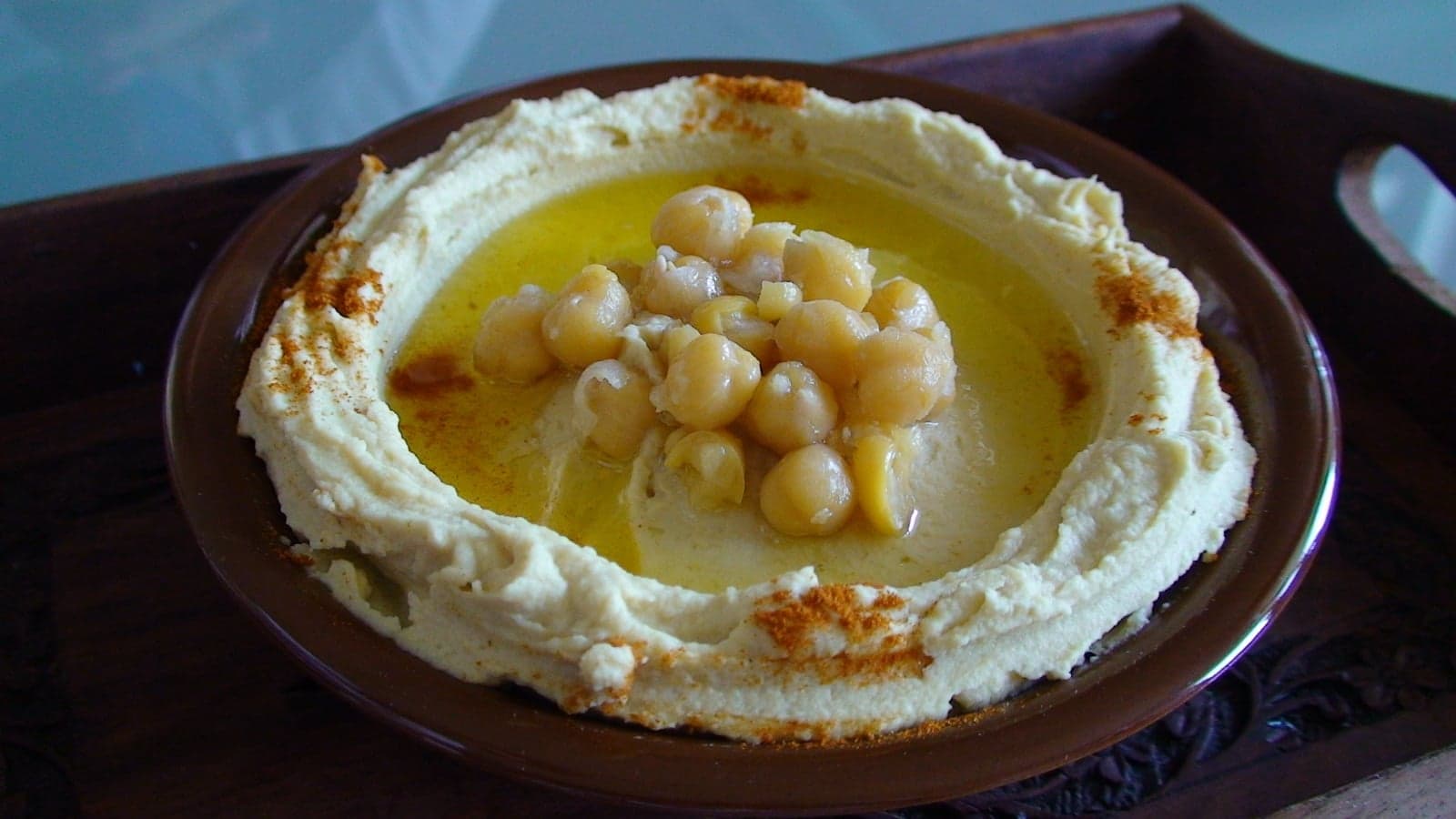 A plate of creamy hummus topped with chickpeas, and a few golden falafel balls
