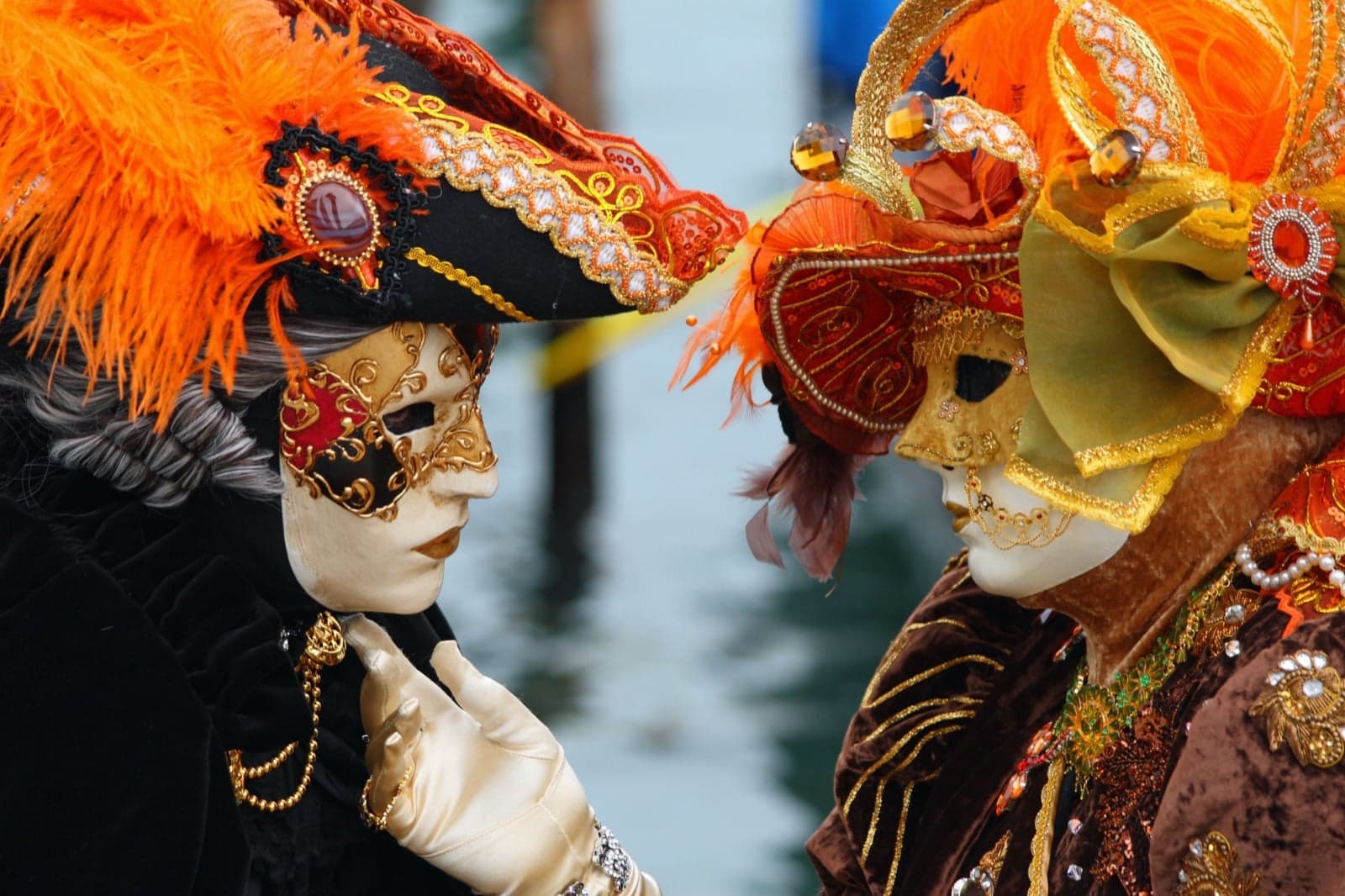 Two people in ornate gold and red Venetian masks and costumes