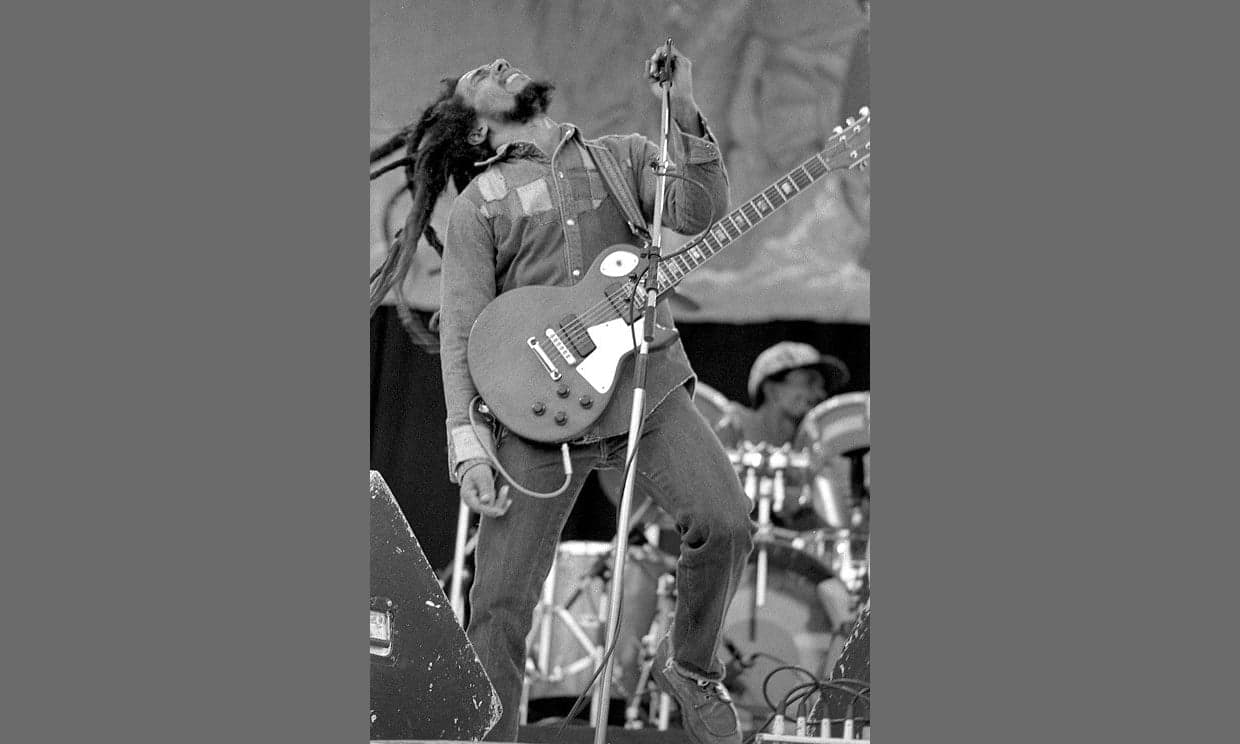 A musician playing guitar at an outdoor reggae concert under palm trees in Jamaica