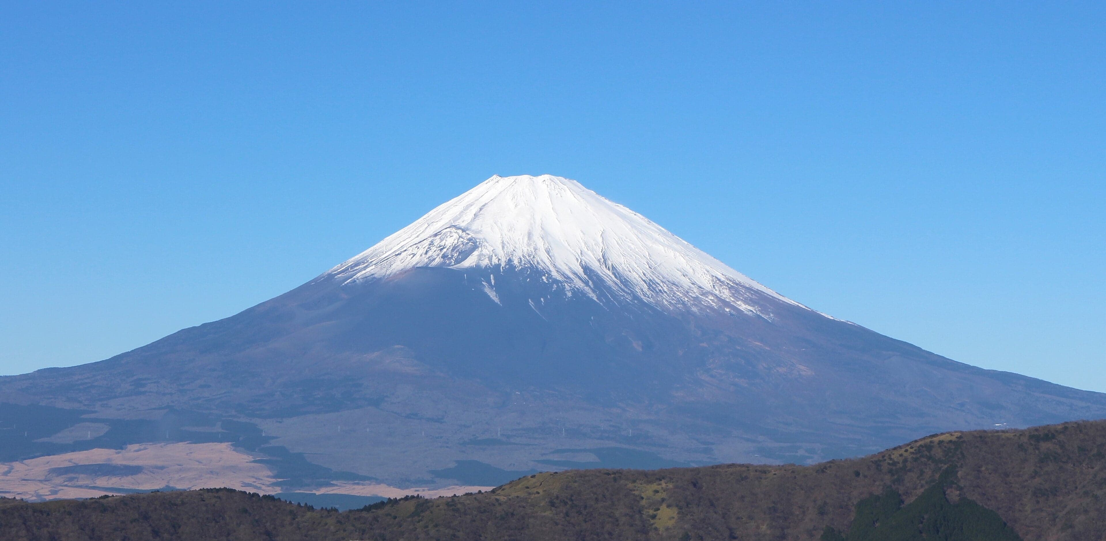 The snow-capped, almost symmetrical cone of Mount Fuji against a clear blue sky