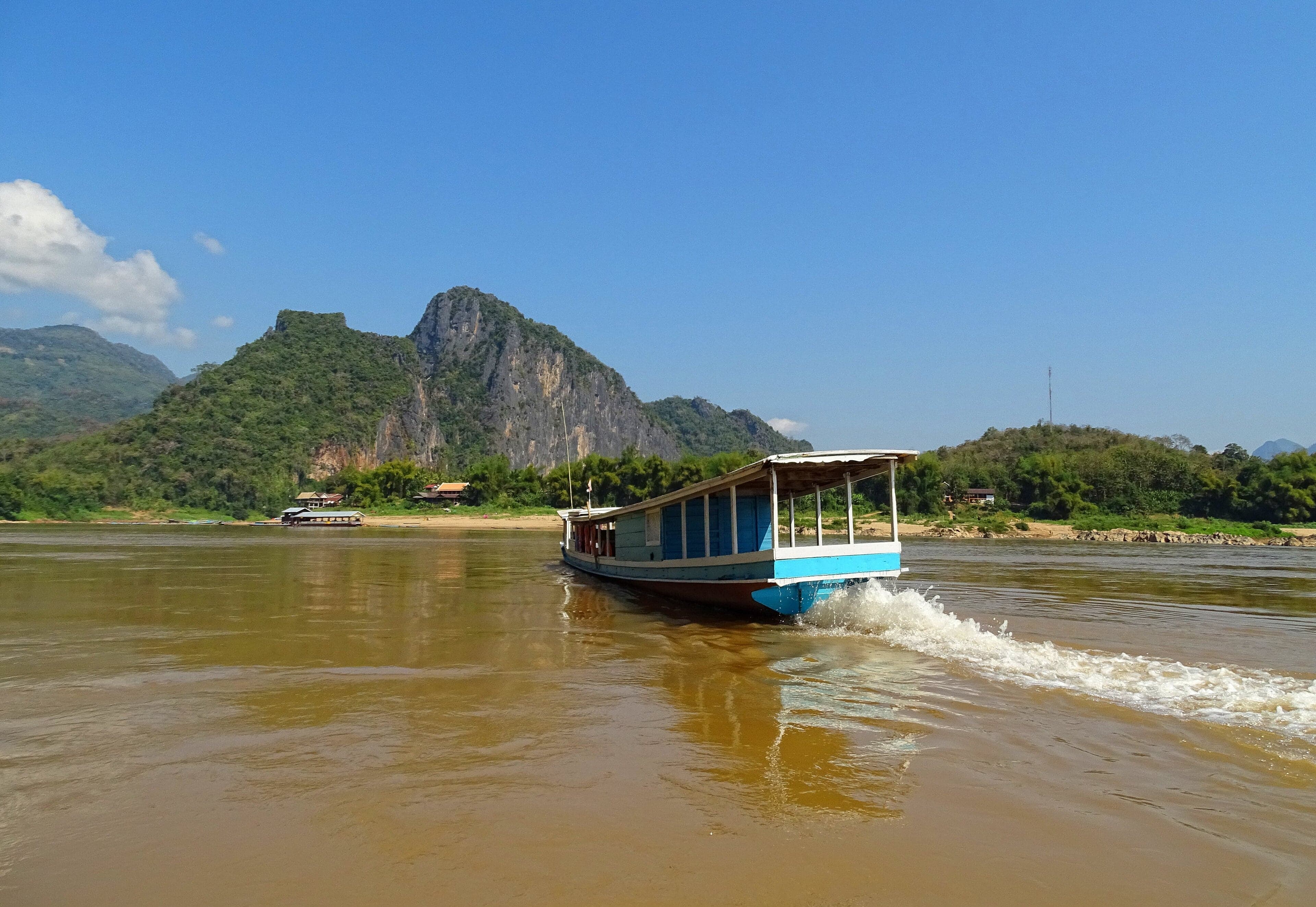 The wide brown Mekong River with green hills and a fishing boat in Laos