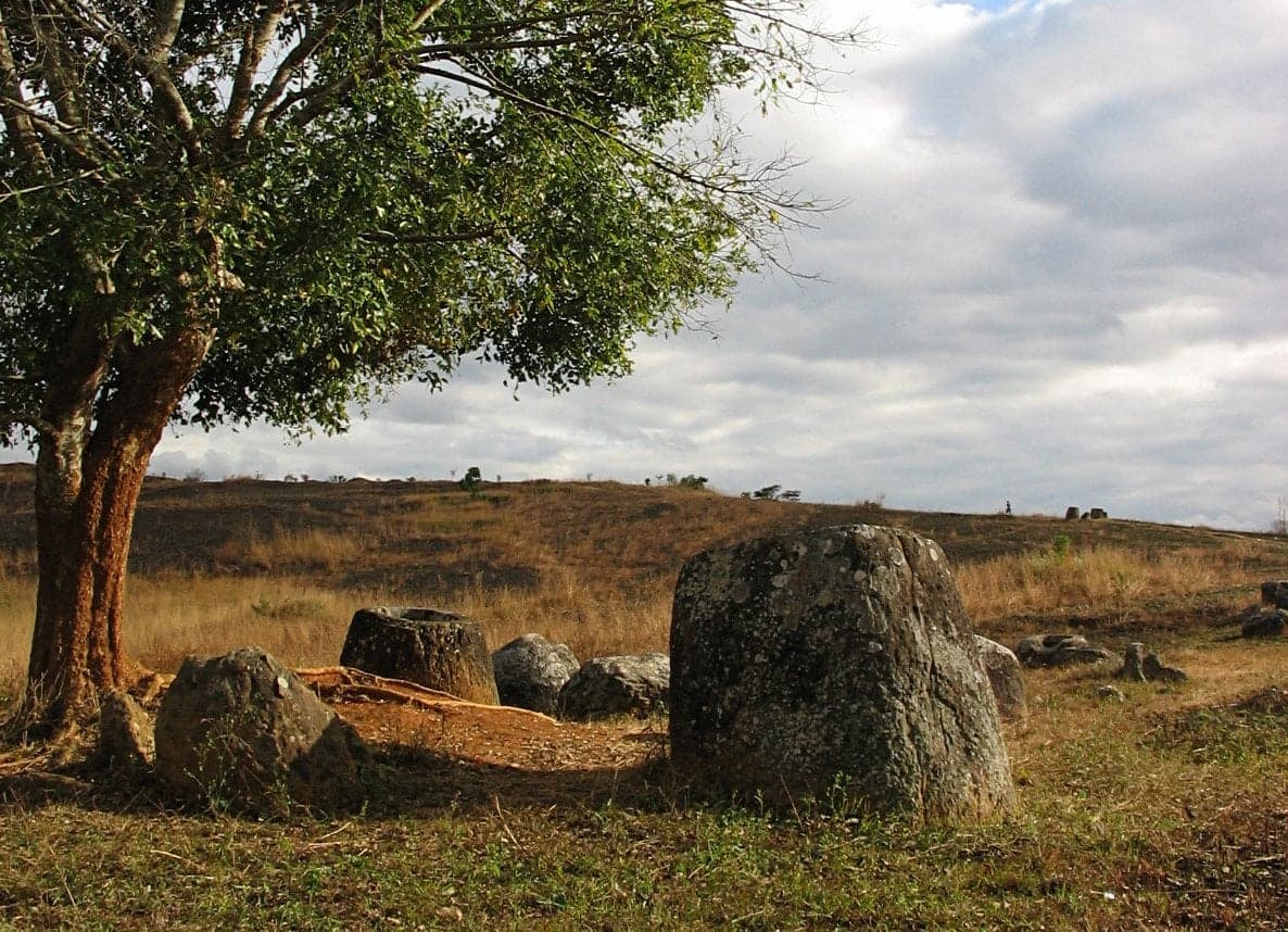 Large ancient stone jars scattered across a green hillside on the Plain of Jars in Laos