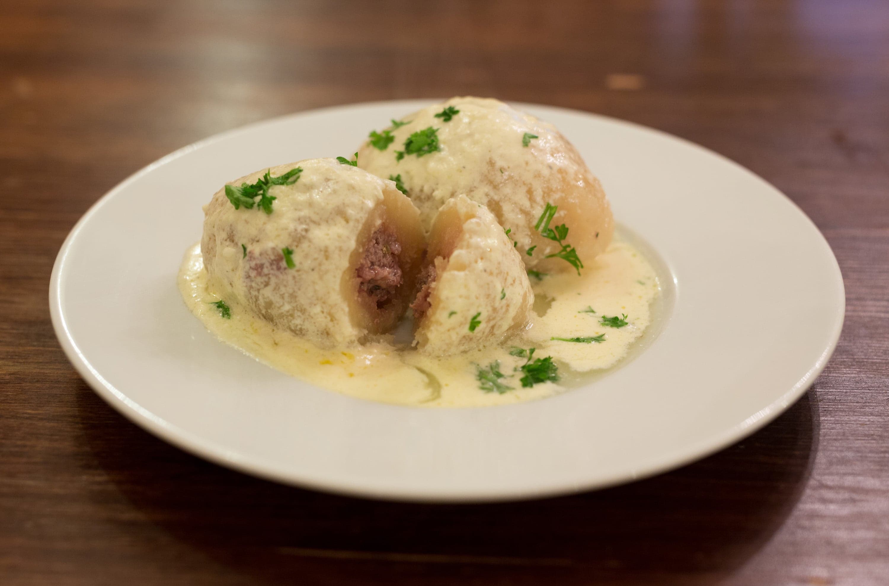 Two large grey oval cepelinai dumplings on a plate topped with sour cream and bacon bits