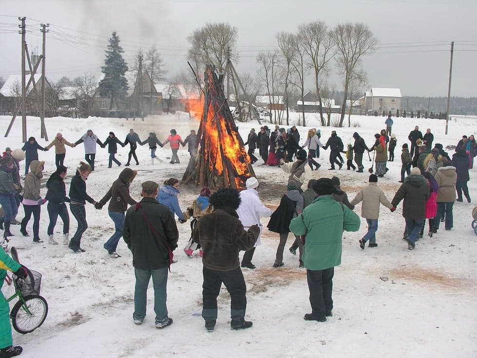 People in colourful folk costumes and frightening masks celebrating Užgavėnės in a snowy village square