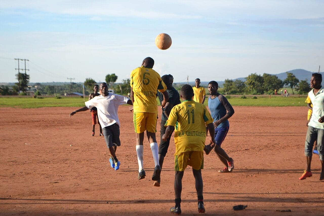 Children playing football on a red dusty pitch in a Malawian village at sunset