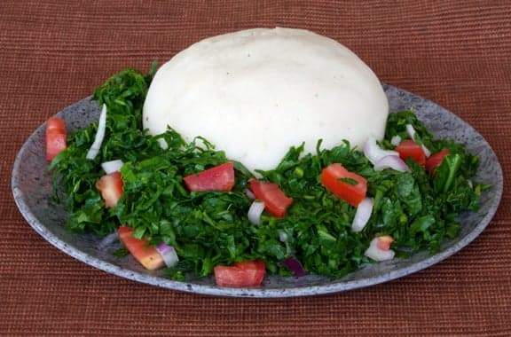 A plate of nsima (white maize porridge) served with green vegetables and grilled fish