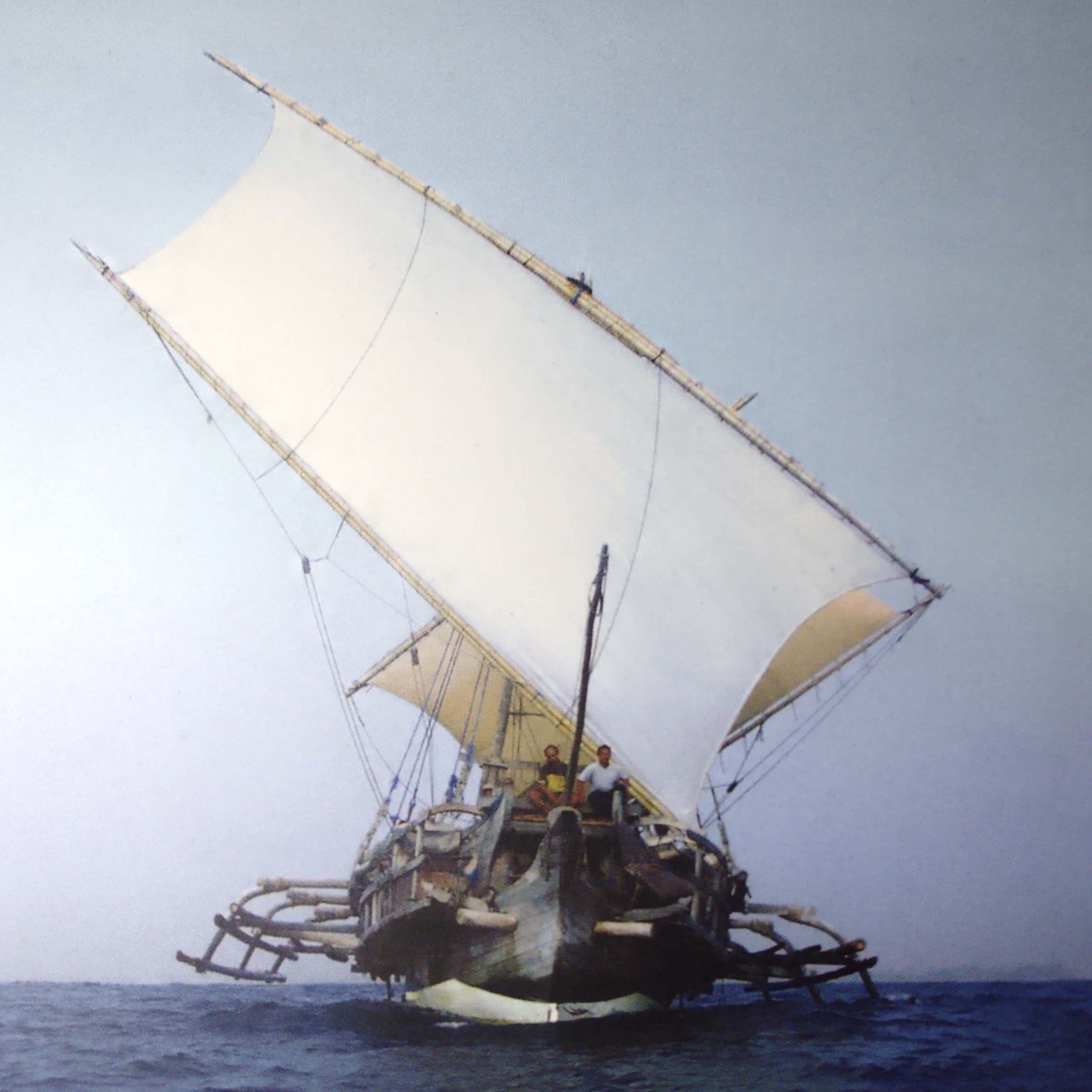 A traditional Marshallese outrigger canoe sailing on bright blue water with a woven sail