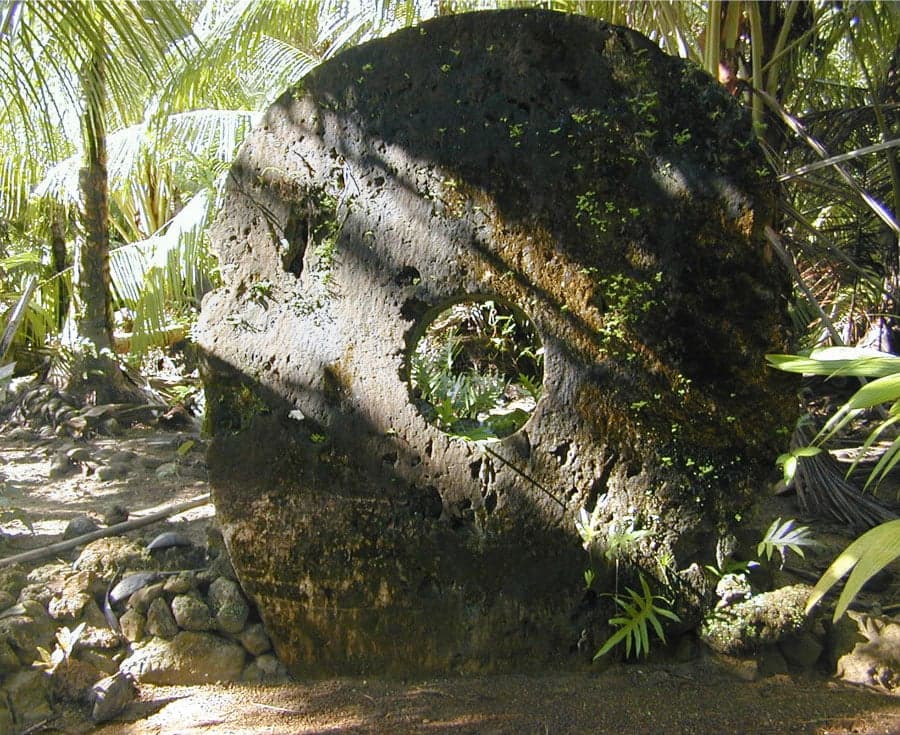 A row of large circular stone discs standing upright against a wall on Yap island
