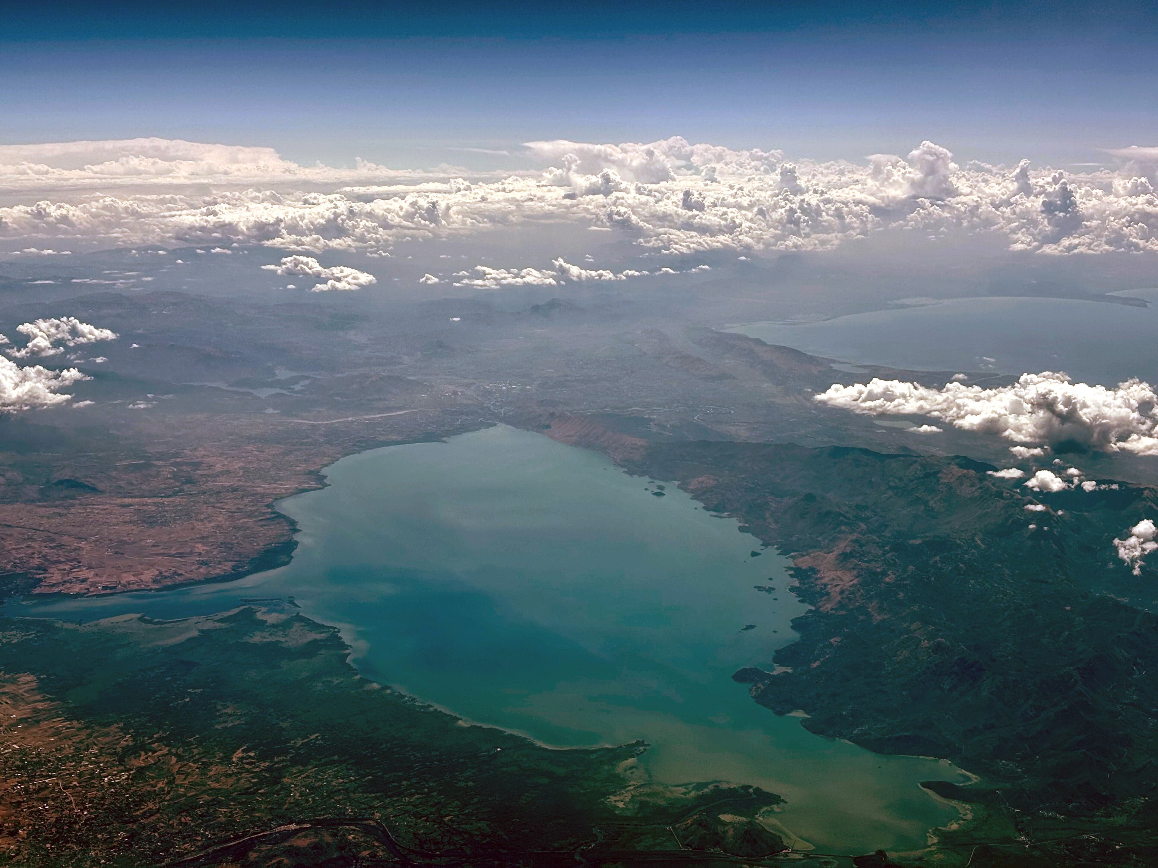 A wide calm lake covered in water lilies with mountains reflected in the surface