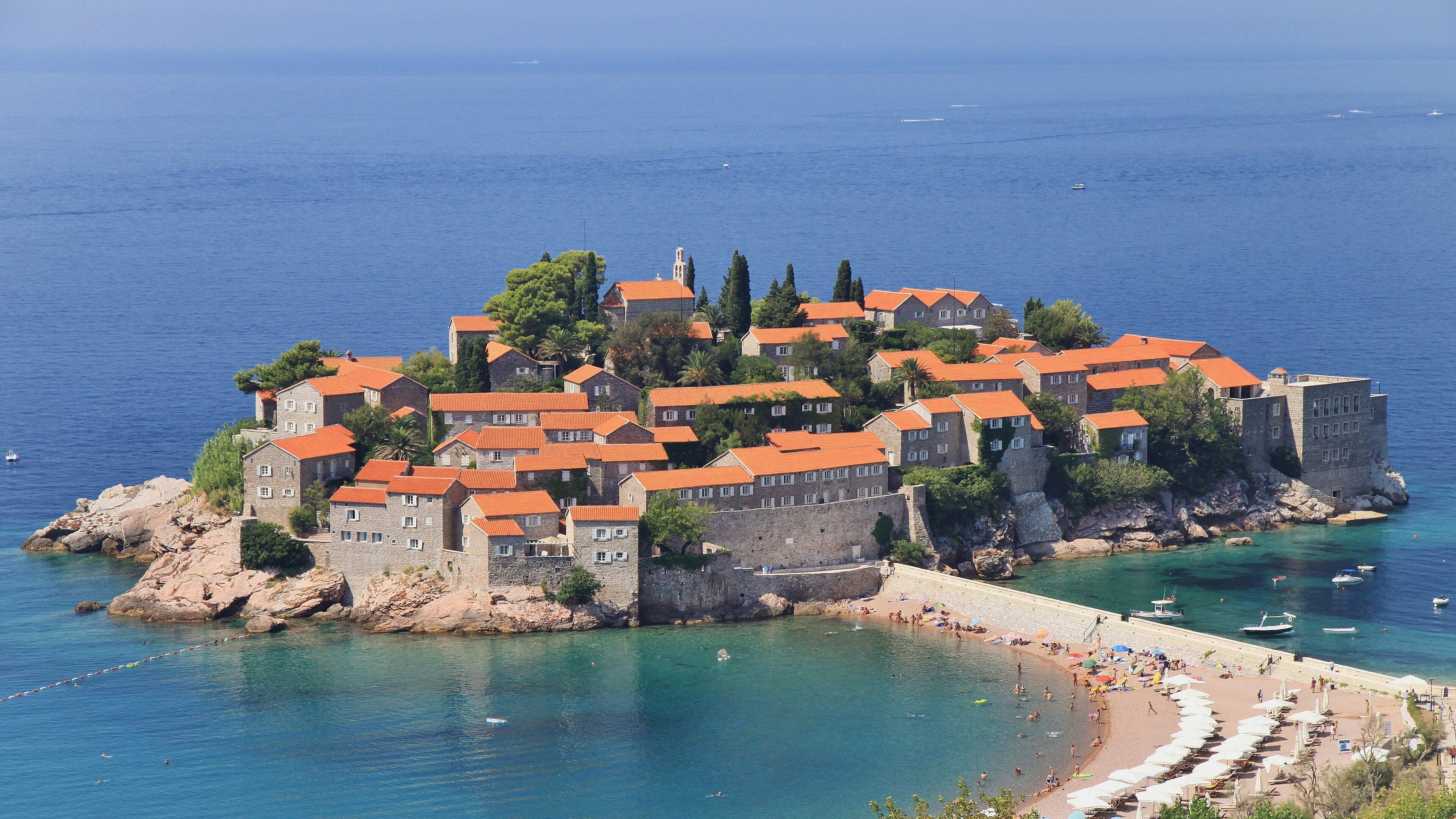 The terracotta-roofed stone buildings of Sveti Stefan island linked to the mainland by a narrow sandy strip