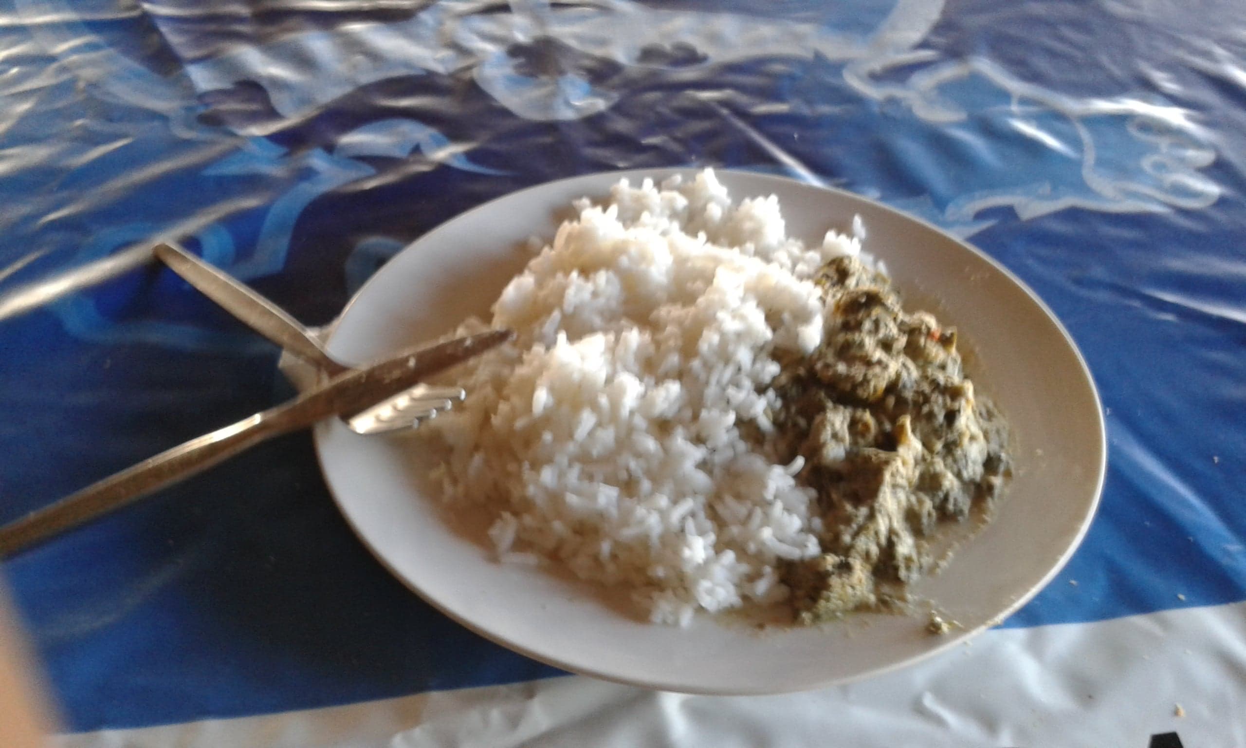 A bowl of green matapa made from cassava leaves and coconut milk with prawns on top