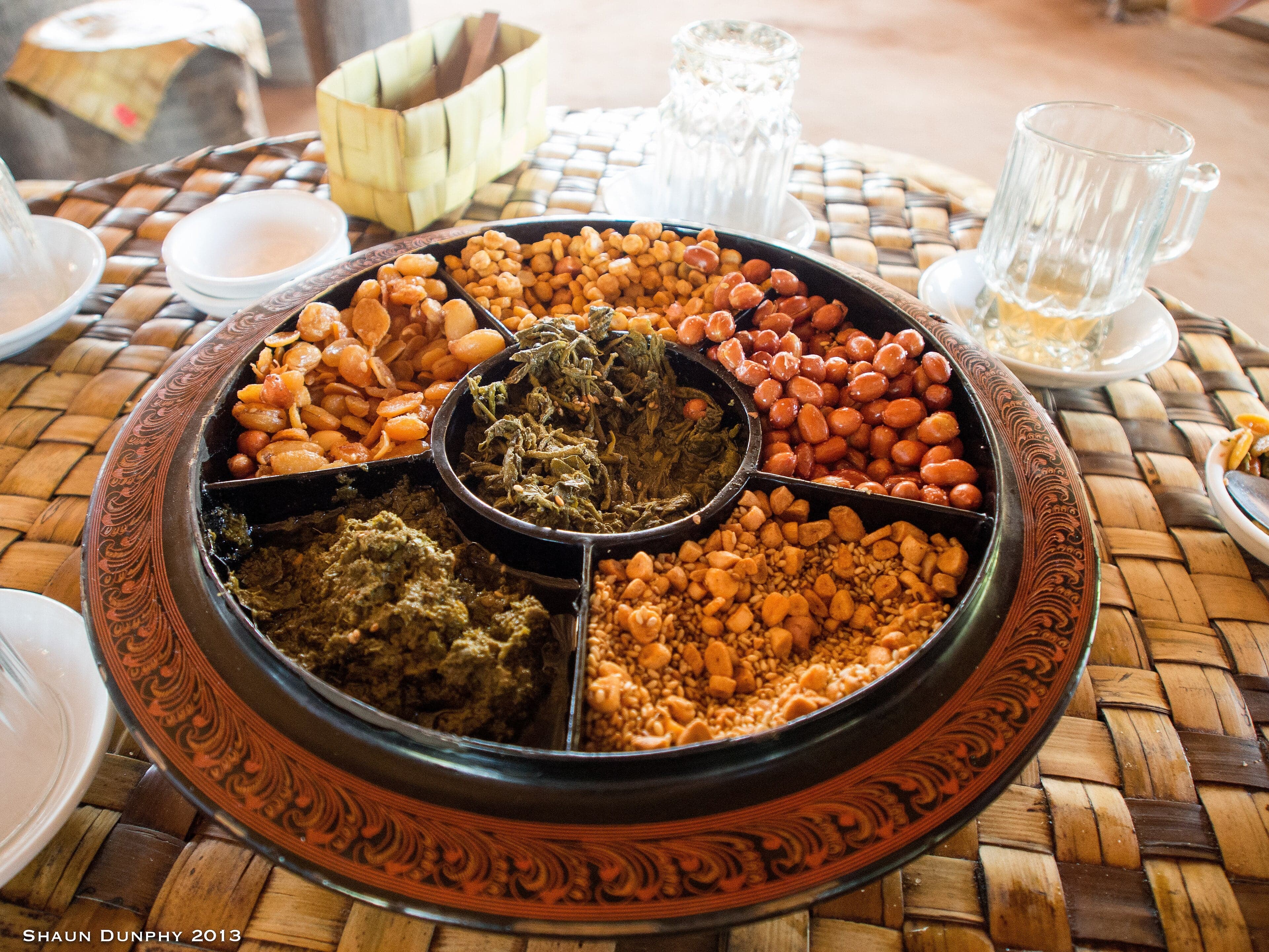 A plate of lahpet thoke with green pickled tea leaves, fried beans, peanuts and tomato