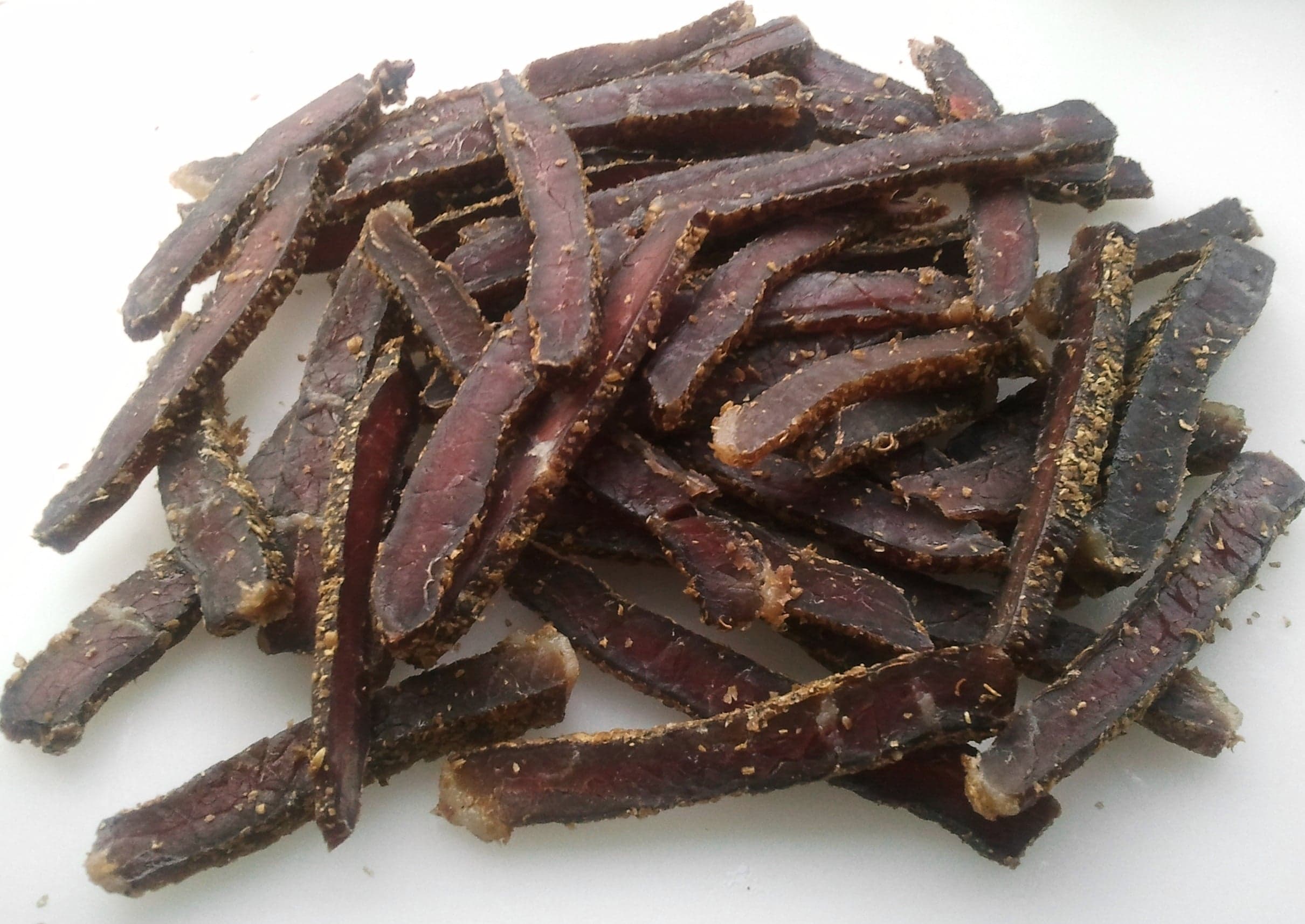 Strips of dark dried biltong meat hanging on a wooden rack