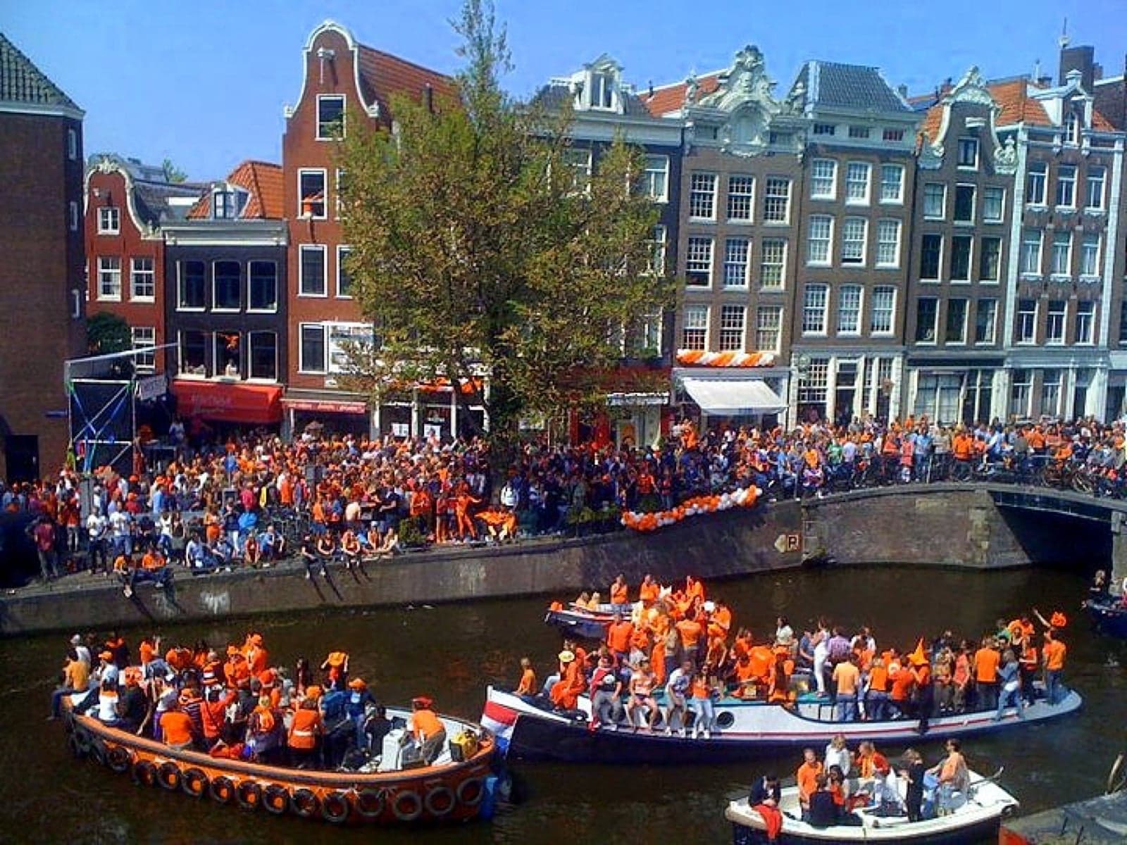 A canal in Amsterdam packed with boats and people all dressed in orange on King's Day